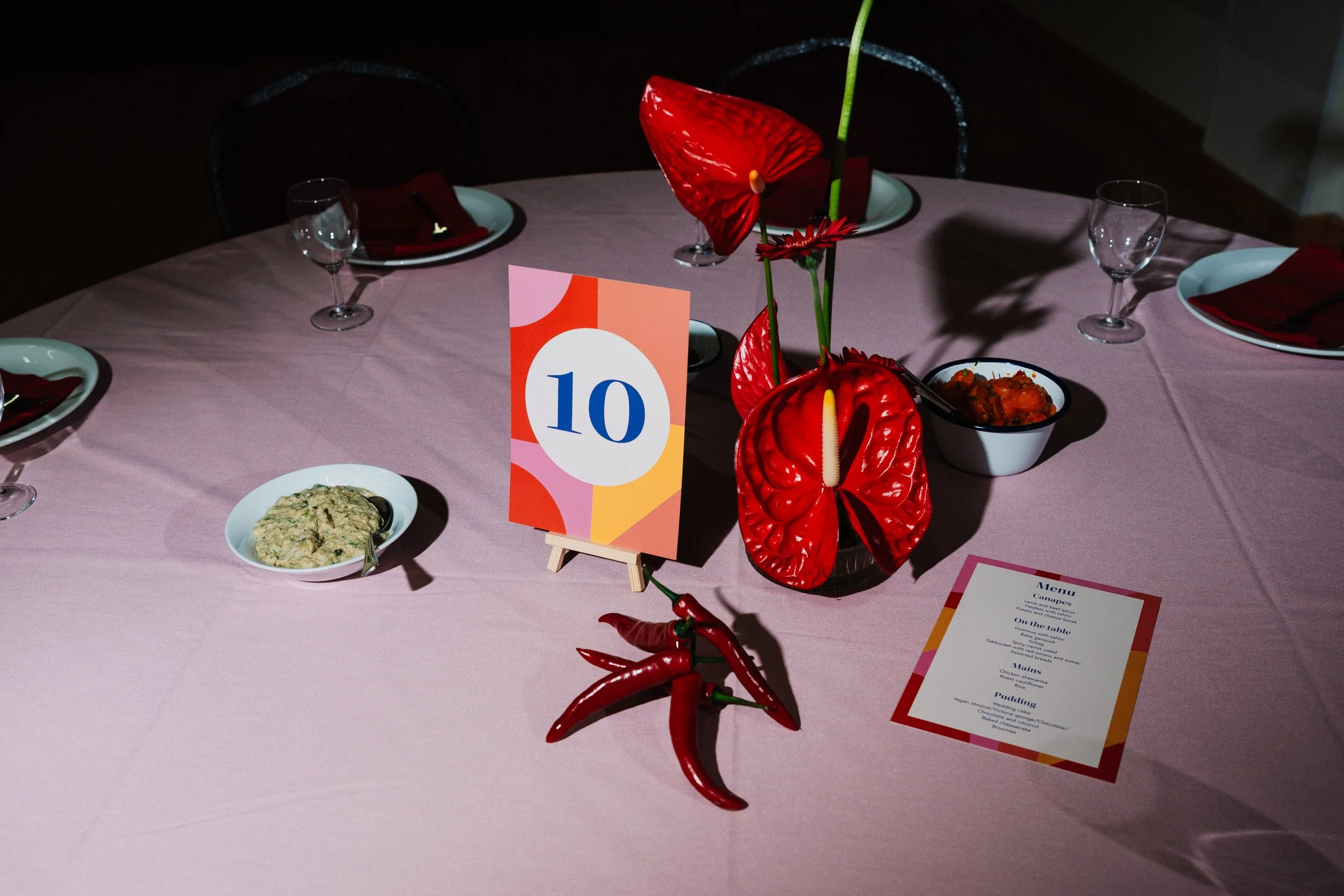 Orange Tree Weddings styling and décor featuring a bold, modern tablescape with graphic table number, vibrant red anthuriums, chilli accents and contemporary stationery, ideal for creative London weddings.