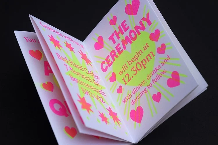 Fun and quirky wedding invitation booklet by Different Day Design Studio, Dorset. Featuring bold neon pink and yellow typography with heart and star motifs, this playful design is perfect for couples planning a vibrant, unconventional wedding celebra