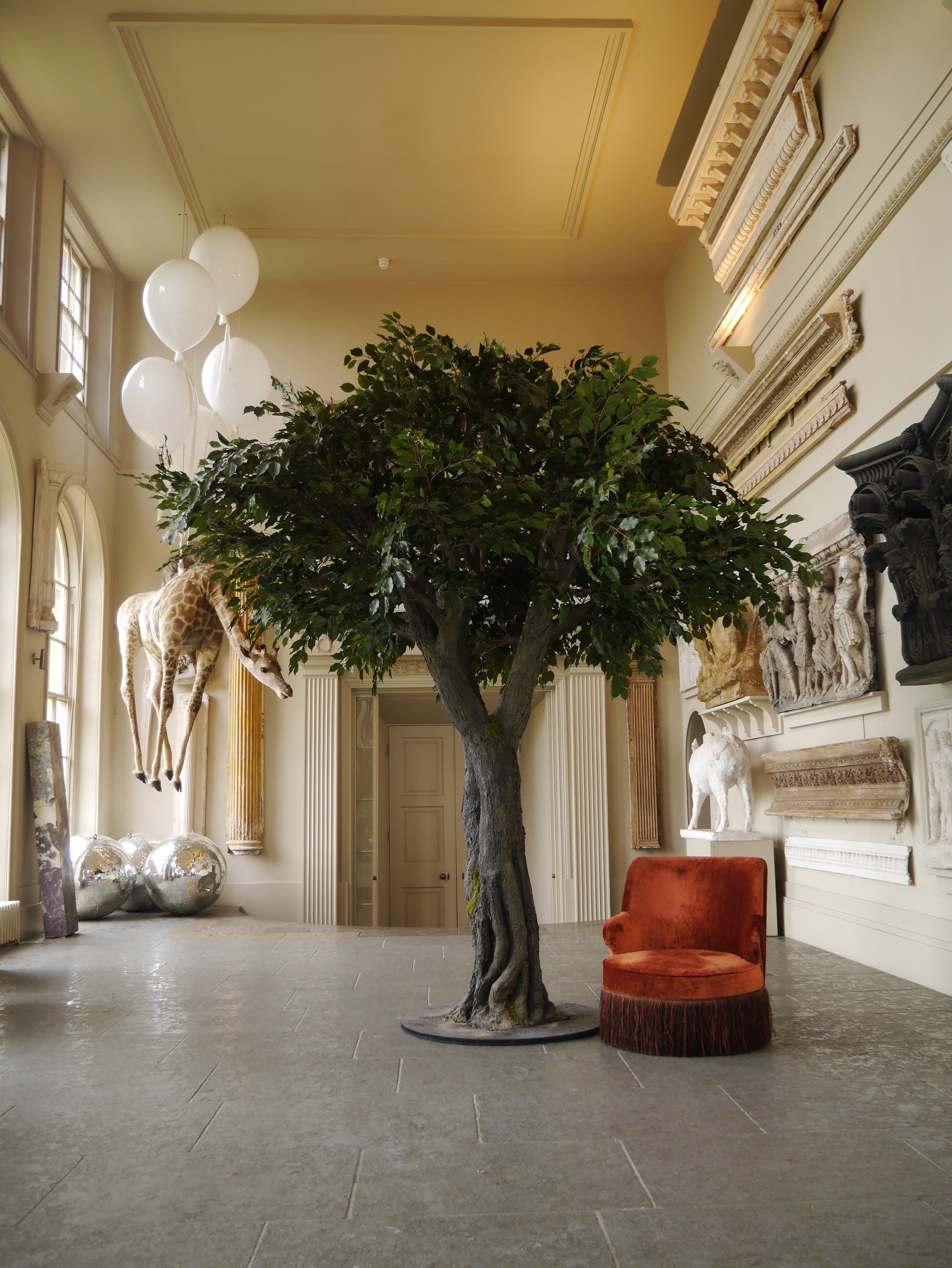 Vowed and Amazed lifelike Tree with an Orange Velvet Chair and a suspended Giraffe! A perfect prop for weddings and late-night celebrations.