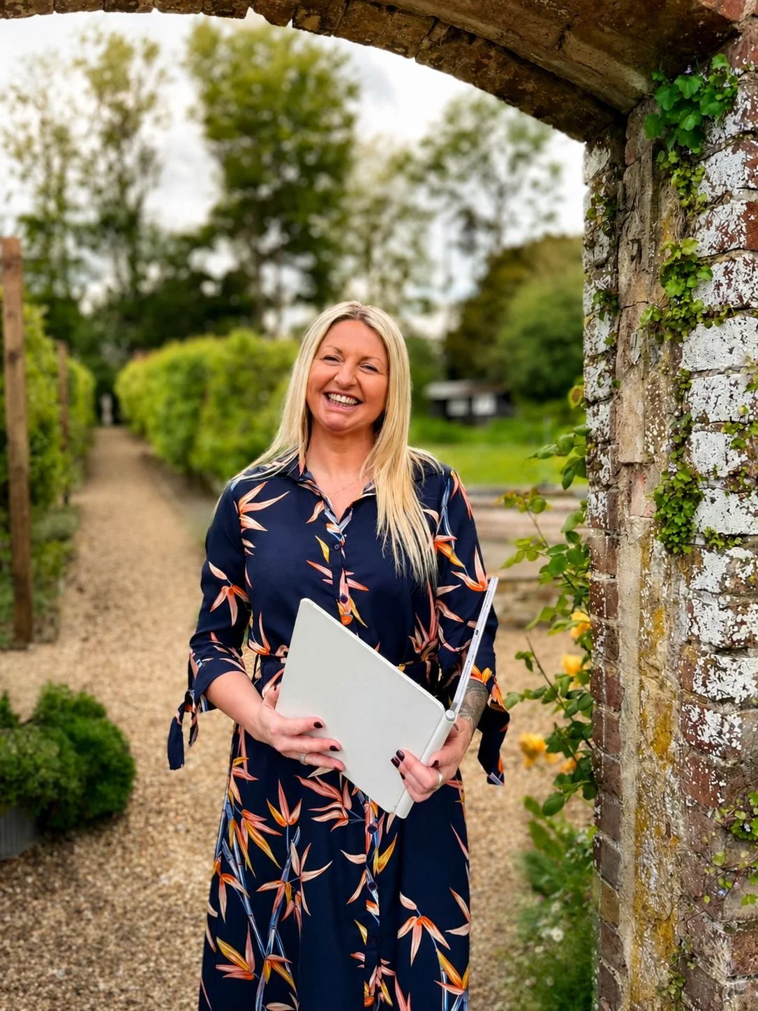 London based wedding celebrant, Ceremonies by Jade, is standing outside and waiting for her couple. She's wearing a navy dress with flowers on it.