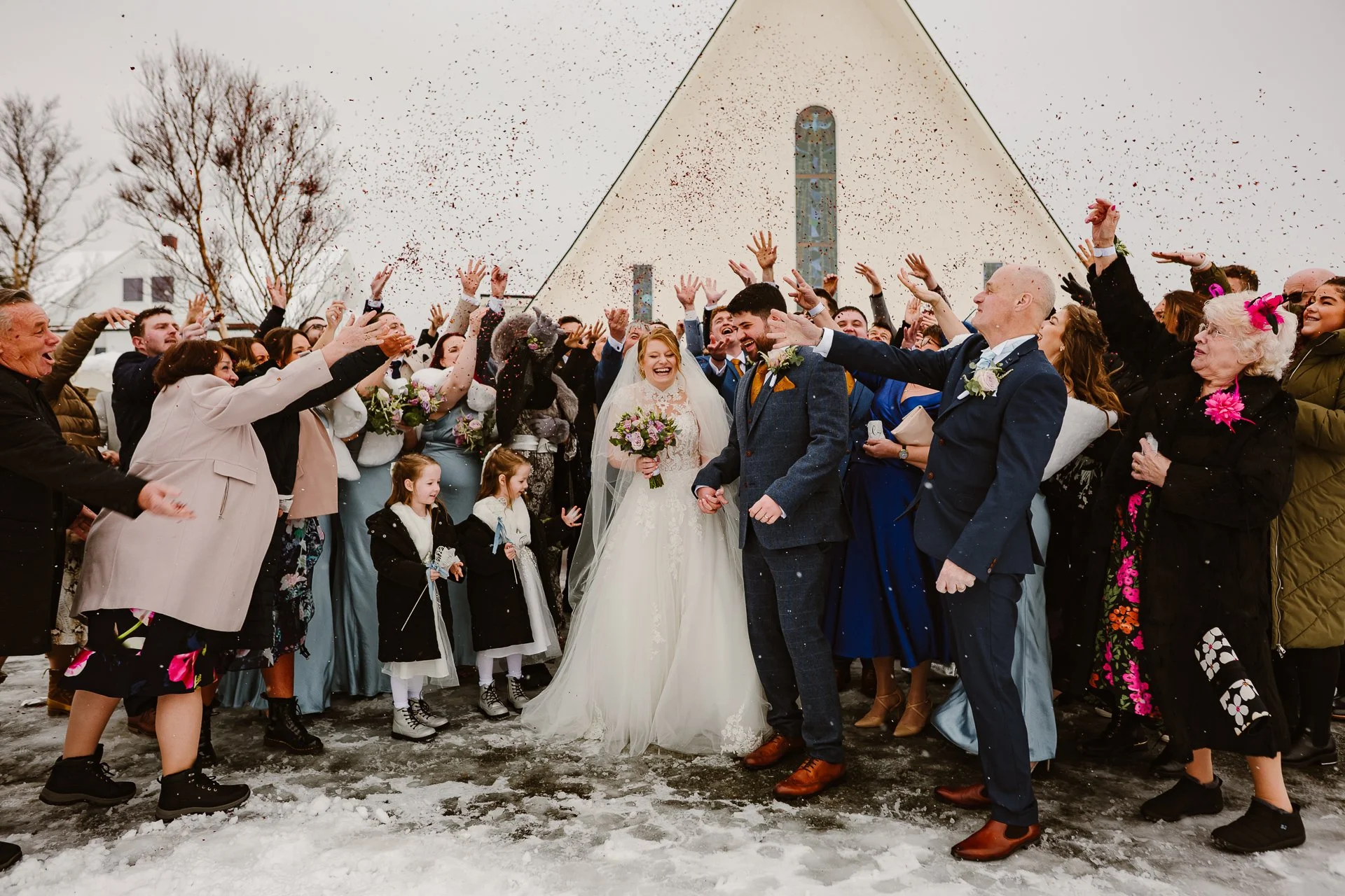 A creative wedding photo showing the bride and groom walking hand in hand, their elongated shadows cast across the sunlit ground. Captured by Bluebell Photo Studio, this artistic wedding portrait highlights golden hour light, natural romance and docu