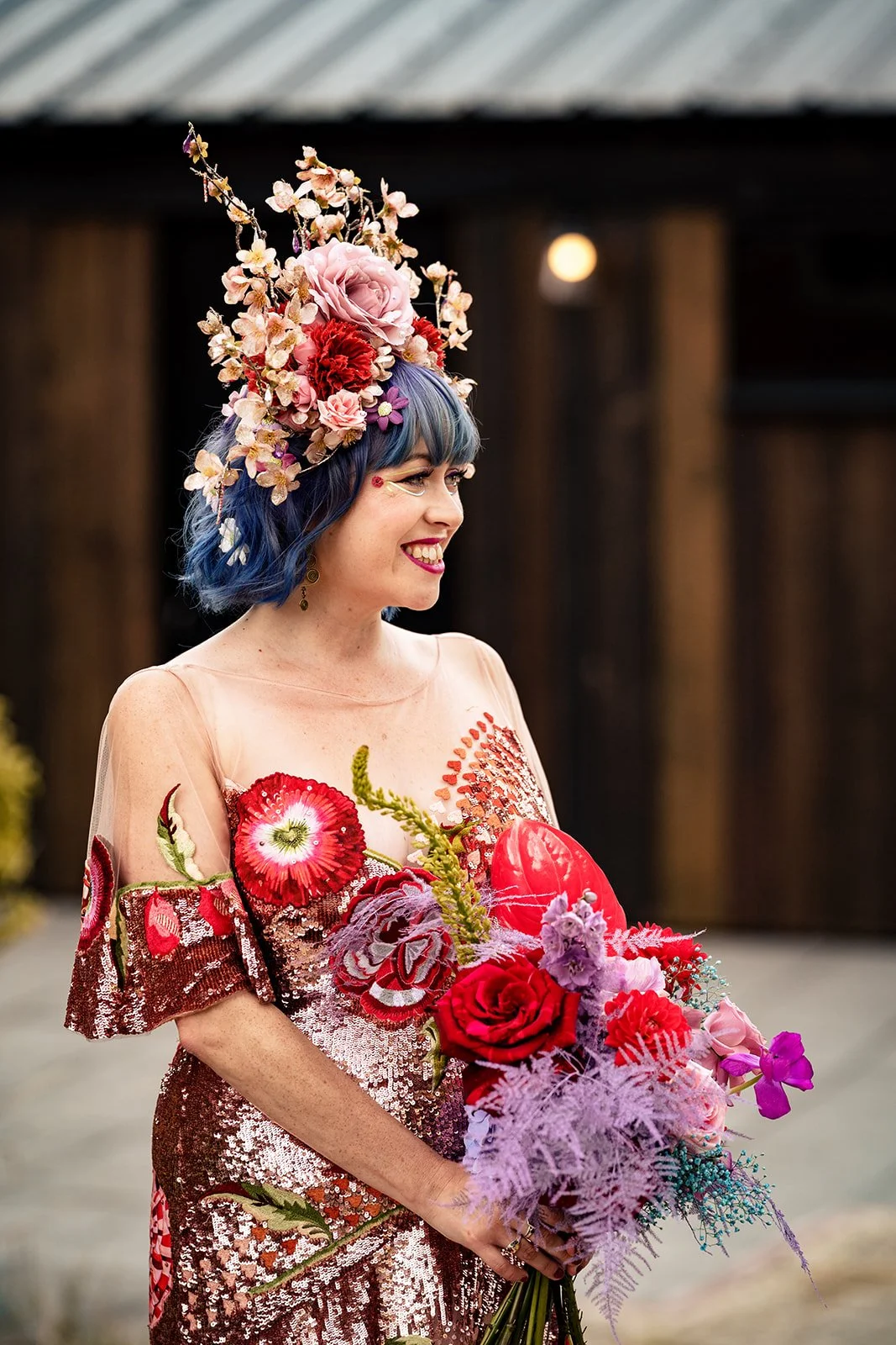 A creative bridal look by Powder Blue Artistry, featuring glowing skin, bold lips, and soft eye makeup that complements the bride’s vibrant floral headpiece and sequin gown. The playful yet polished beauty styling enhances the colourful, artistic fee
