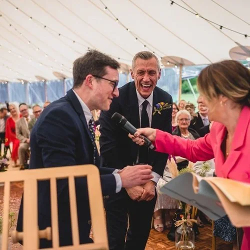 Wedding celebrant Vicky engaging guests with a microphone during a lively and interactive ceremony under a marquee.
