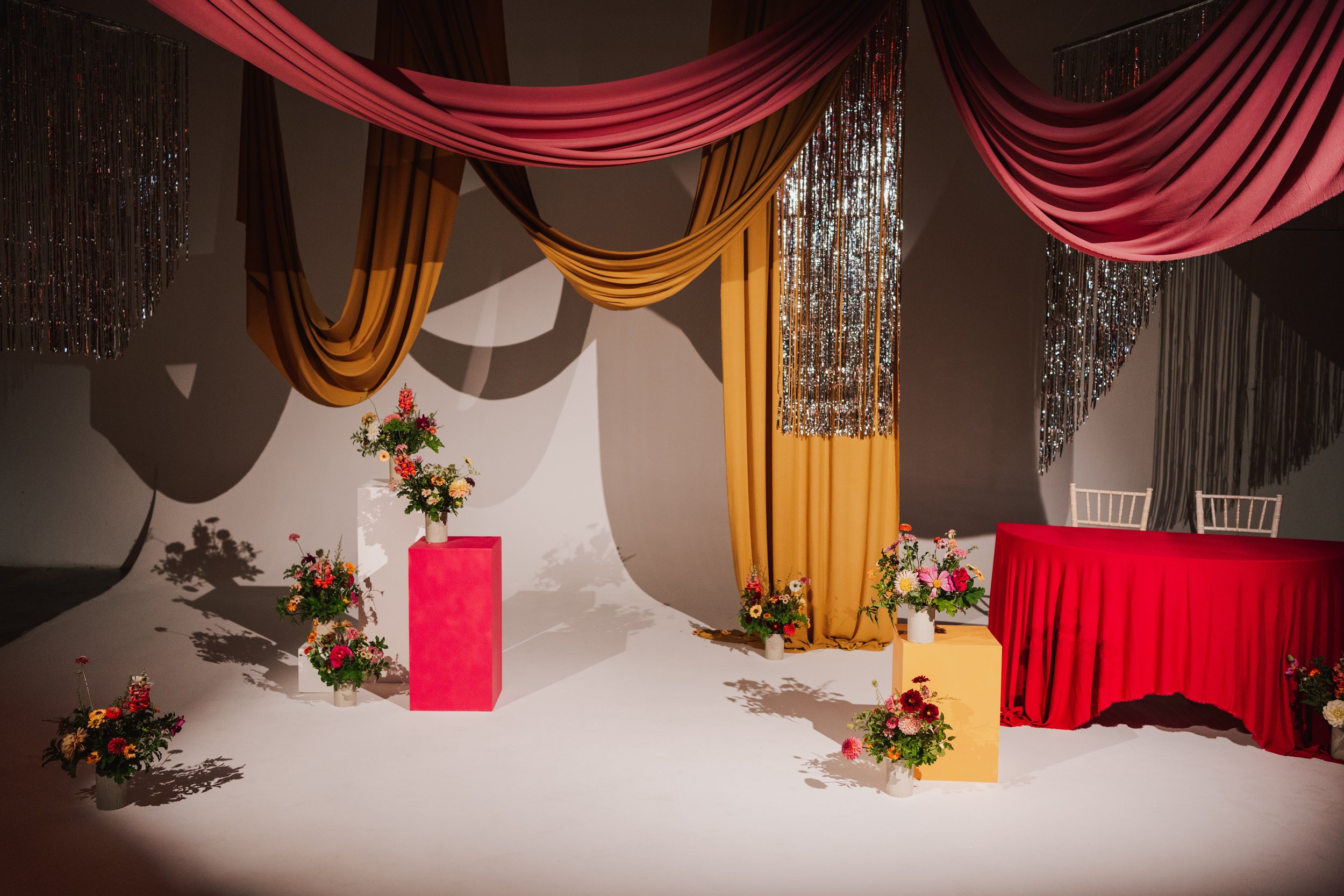 Orange Tree Weddings styling and décor featuring rich draped fabrics, shimmering metallic backdrops and bold floral arrangements, creating a modern, art-led wedding ceremony setting with striking colour and texture.
