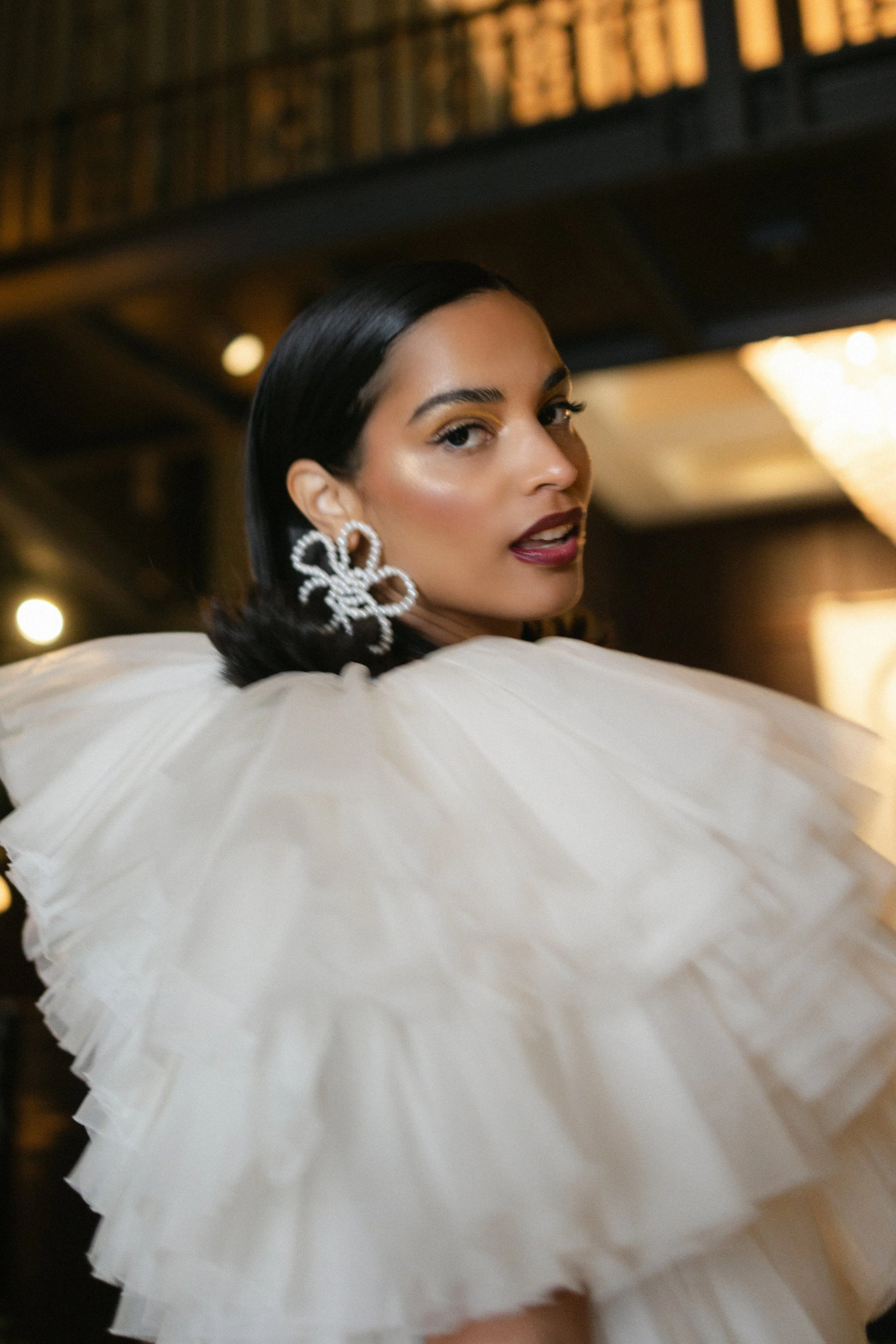 A high-fashion bridal look by Powder Blue Artistry - glowing skin, sculpted cheekbones, and a deep berry lip paired with gold-toned eyeshadow. The sleek hair and statement pearl earrings elevate the look, perfectly balancing drama and elegance for a 