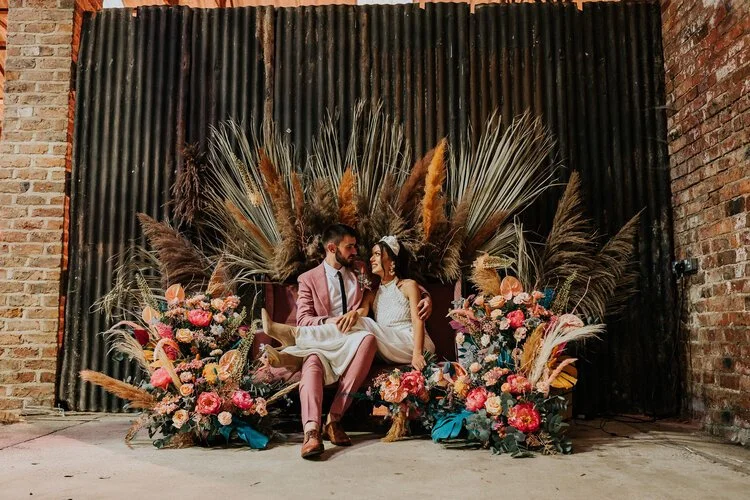 A newlywed couple shares a quiet, intimate moment surrounded by stunning boho-inspired florals and pampas grass at White Sykes Fields. The earthy tones, rustic textures, and vibrant blooms create a dreamy backdrop that perfectly complements the coupl