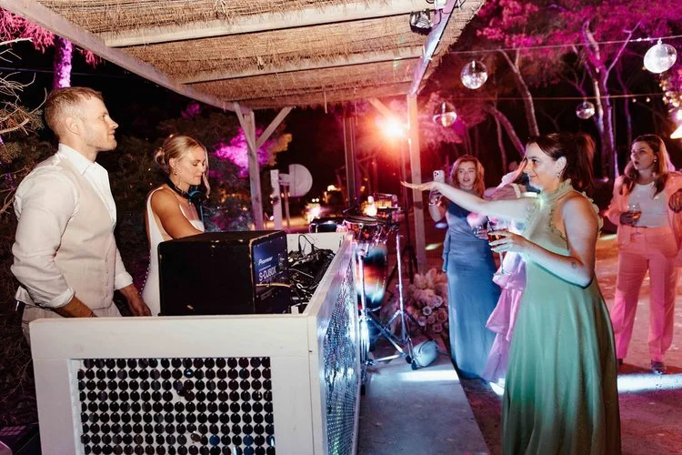 Mr and Mrs L performing at an outdoor reception while guests dance and celebrate under disco balls and colourful lighting. The lively setup blends professional sound equipment with a fun festival-style atmosphere, perfect for couples wanting high-ene
