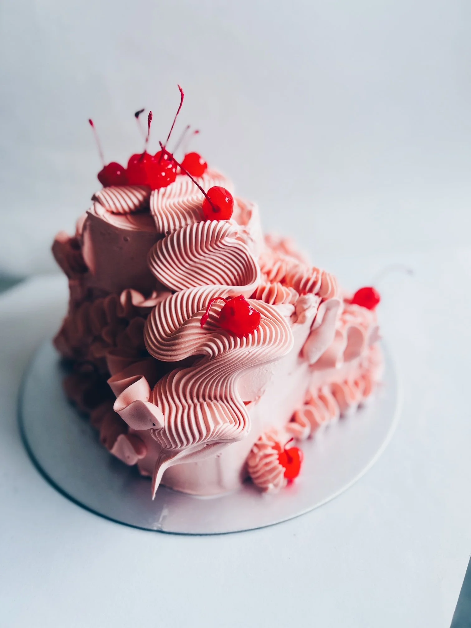 A pink cake with red cherries by Sarah and Cake.