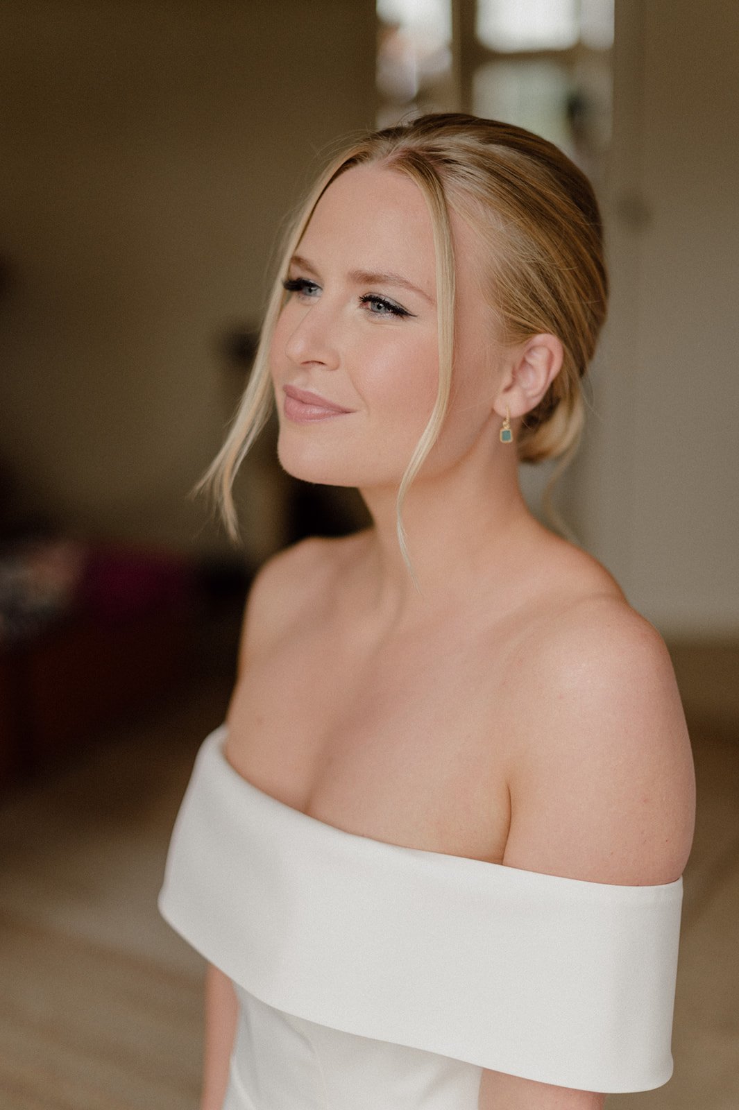 A timeless bridal portrait featuring makeup by Powder Blue Artistry, with soft glowing skin, defined eyes, and a natural pink lip. The elegant and understated beauty look complements the bride’s classic off-the-shoulder gown, perfect for modern and r