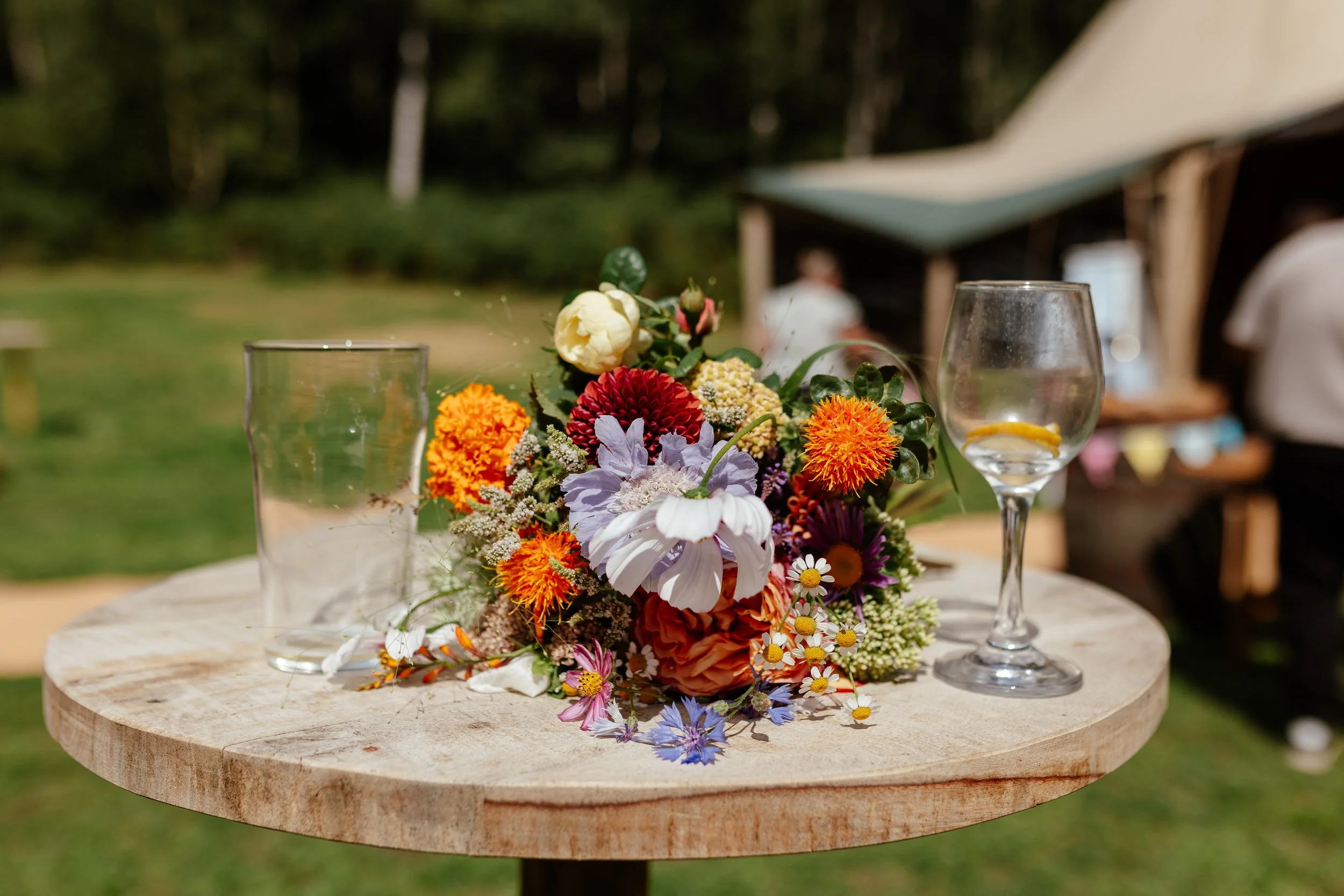 A table at an outdoor wedding with flowers and empty glasses.