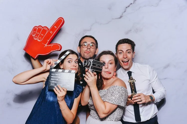 A fun group of wedding guests posing with movie-inspired props in the Flash Fox Photo Booth, complete with a marble-style backdrop. This creative setup captures the joy and laughter of the celebration, giving everyone a keepsake to remember. Flash Fo