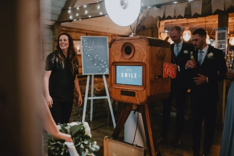 A beautifully lit wedding reception featuring the Flash Fox Photo Booth in action. Guests gather around the stylish wooden booth, ready to capture fun and candid moments. Its vintage-inspired design fits perfectly with rustic UK wedding venues, bring