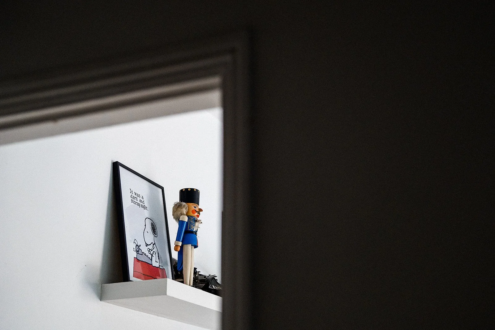 A picture of snoopy on a shelf next to a Nutcracker soldier.