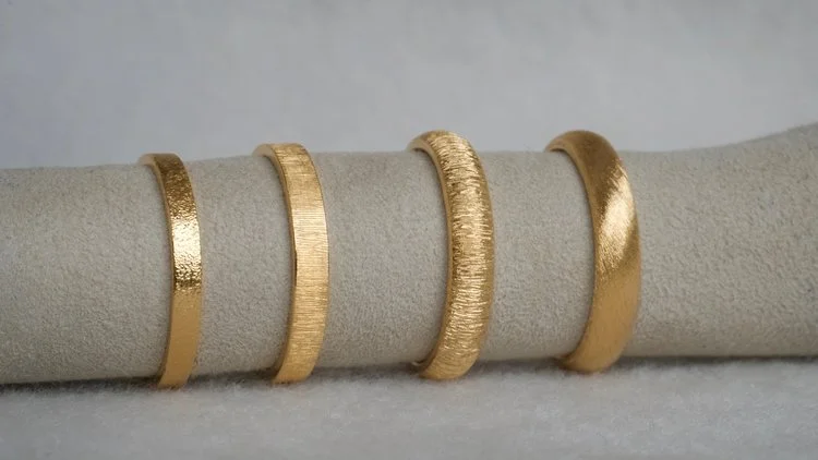 A collection of Natalie Vernazza handcrafted gold wedding rings displayed side by side, showcasing a range of subtle textures and finishes, from brushed and matte to softly hammered, highlighting timeless, modern wedding jewellery design.