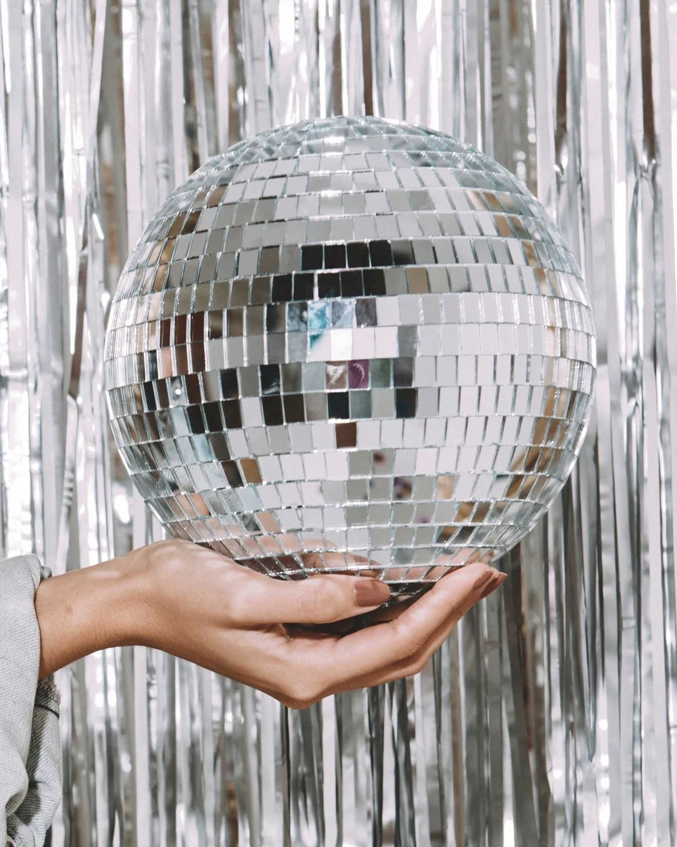 A hand holding a disco ball in front of a silver curtain.