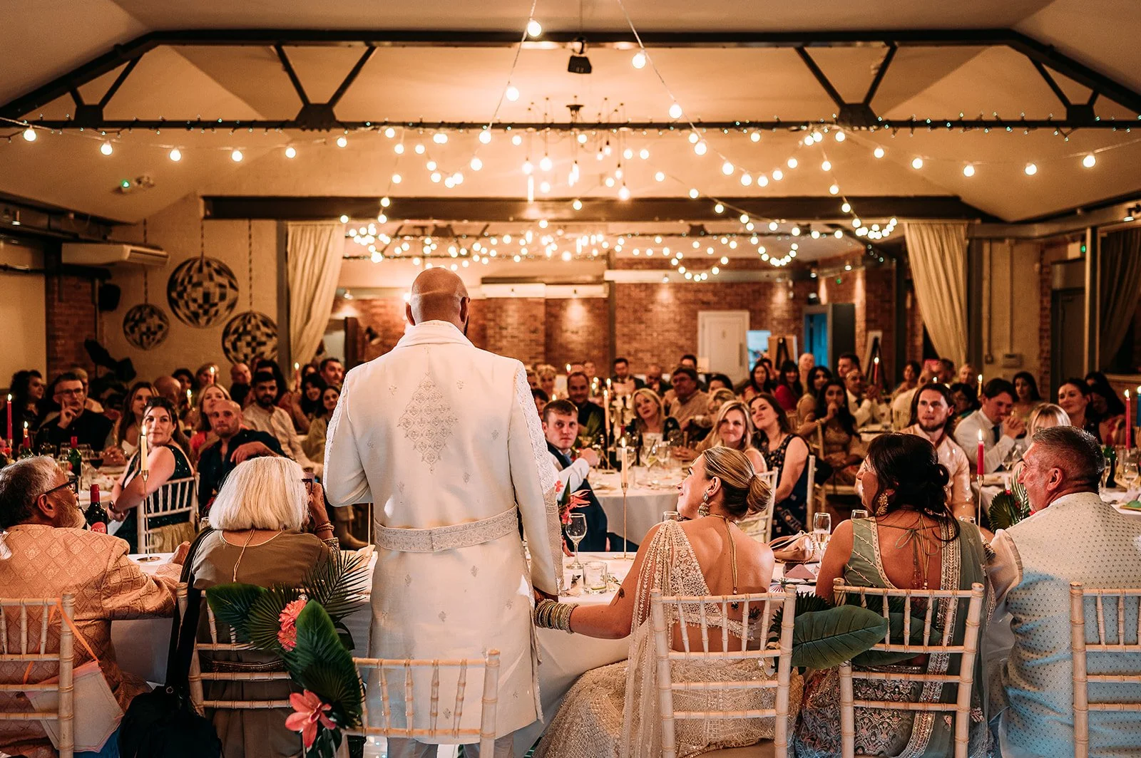 A modern wedding reception inside New Craven Hall in Leeds. There are industrial beams and fairy lights.