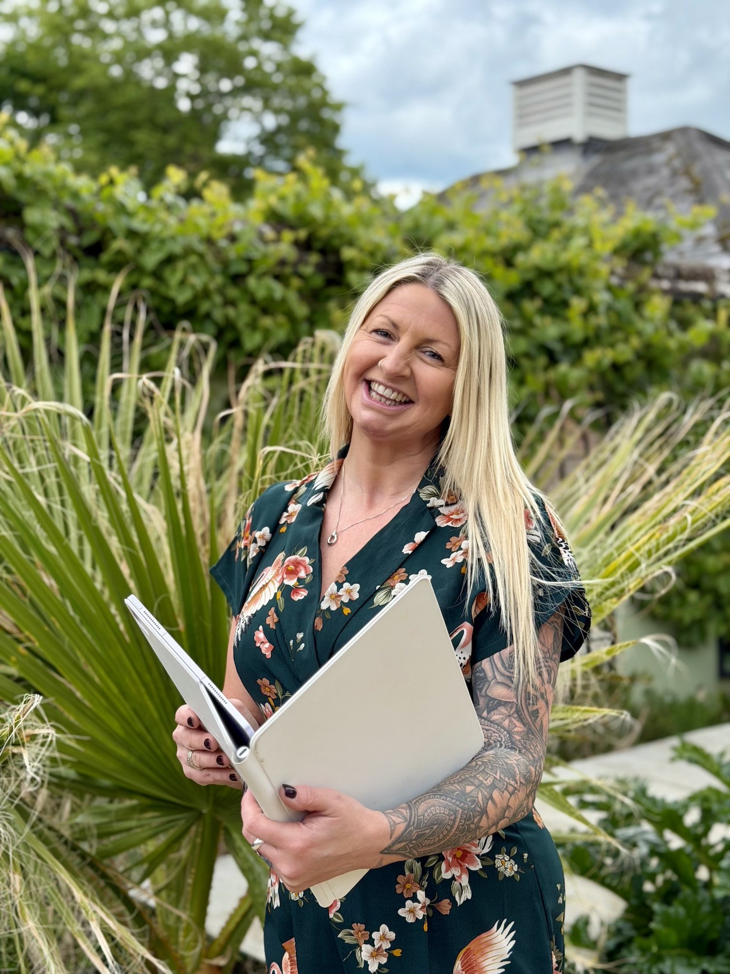 A photo of a blonde wedding celebrant called Jade. She is outside and wearing a floral dress.