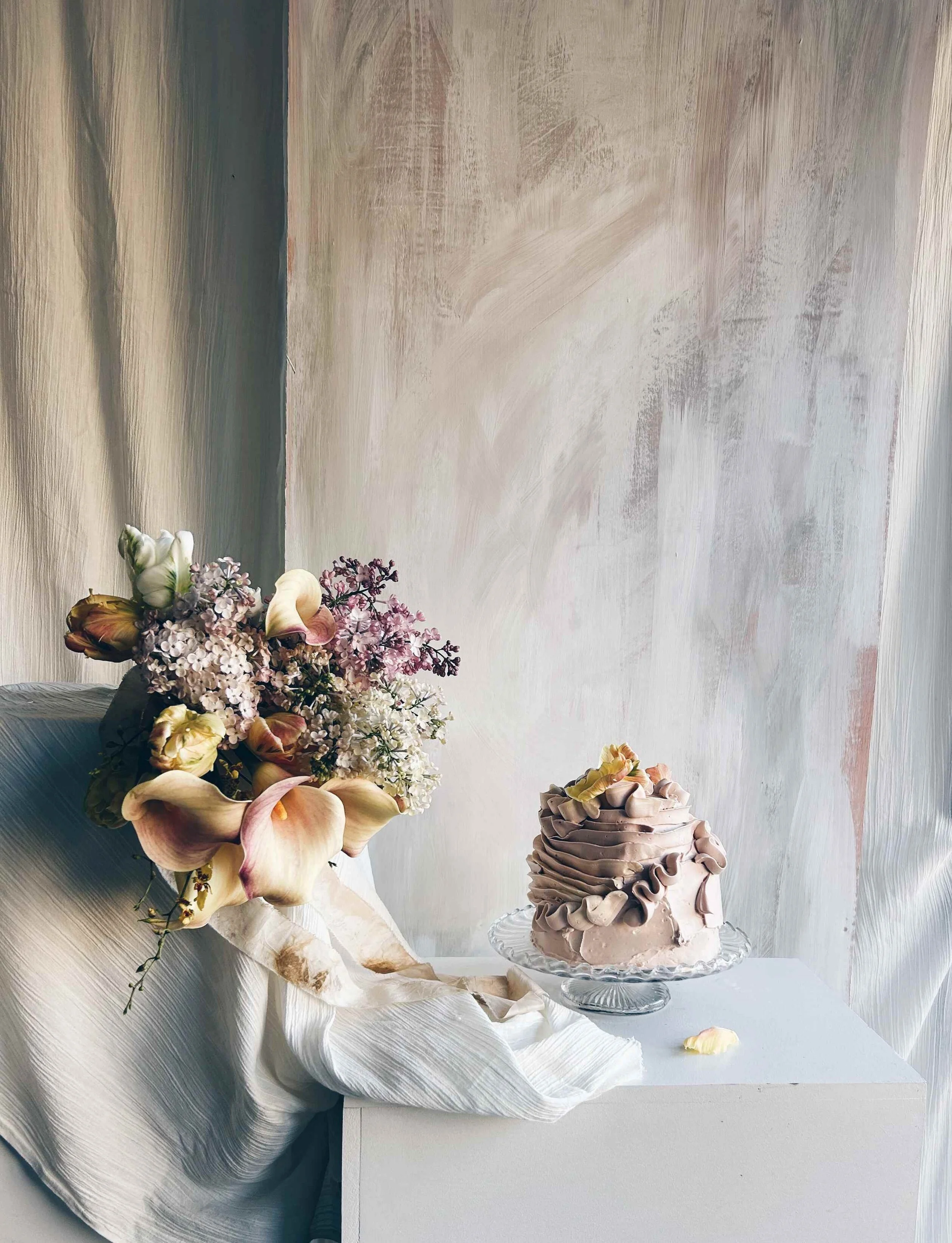 An artistic wedding cake by Sarah and Cake. It's sitting next to an artistic bridal bouquet and looks like a work of art.