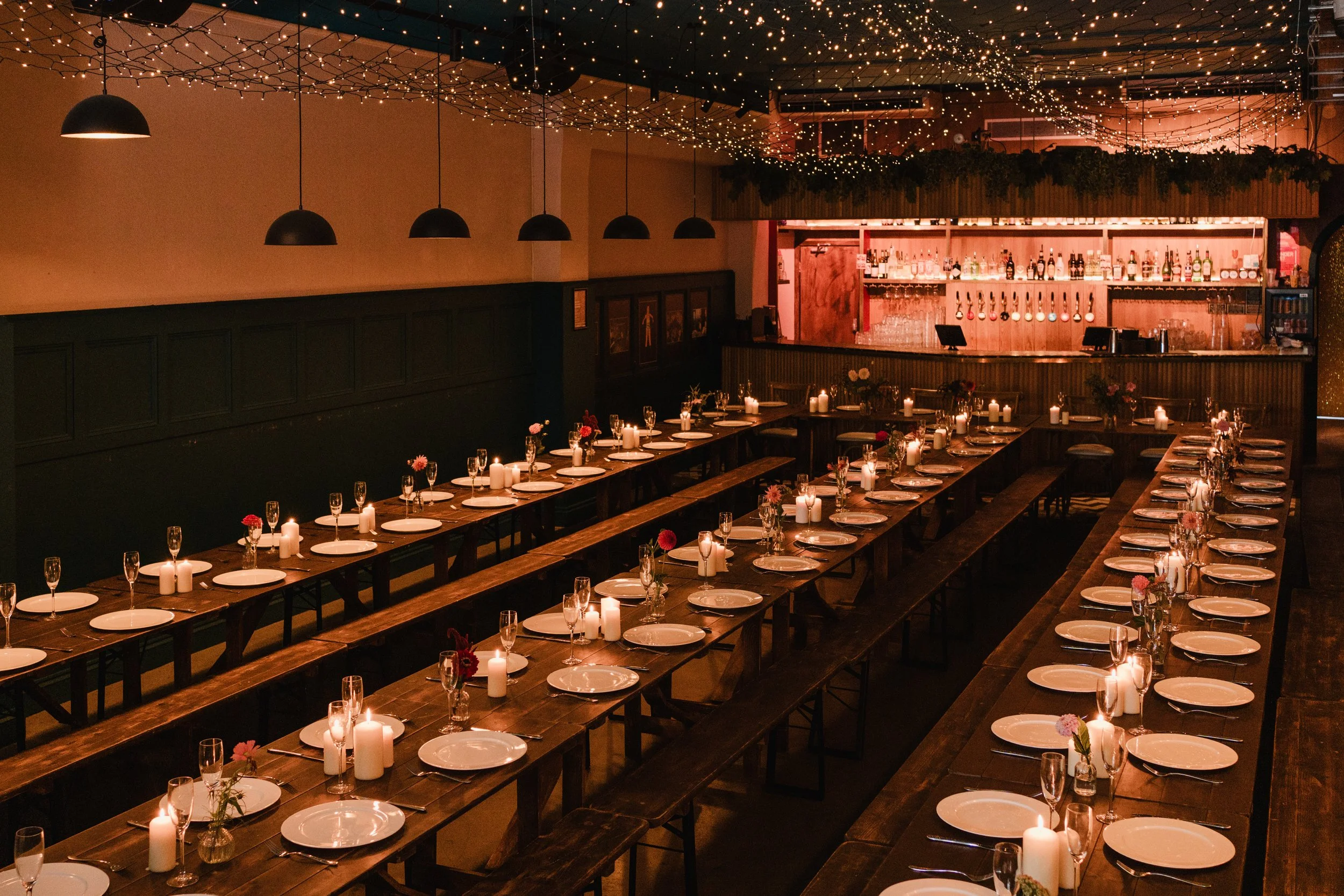 Contemporary wedding reception setup at Colours Wedding Venue in Shoreditch, London, featuring long banquet tables, warm candlelight and a stylish bar for a modern, intimate city celebration.