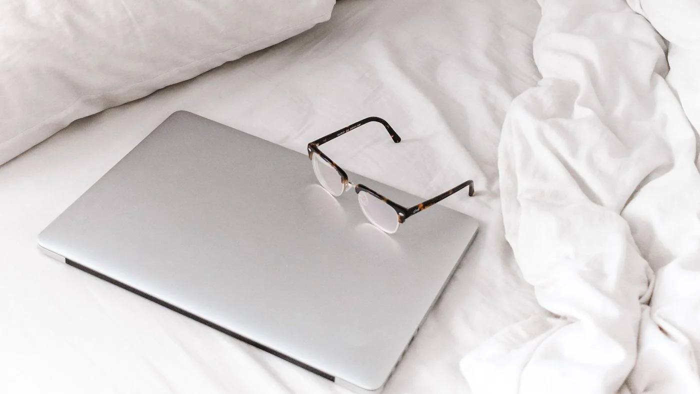 A wedding supplier's laptop and glasses on their bed.