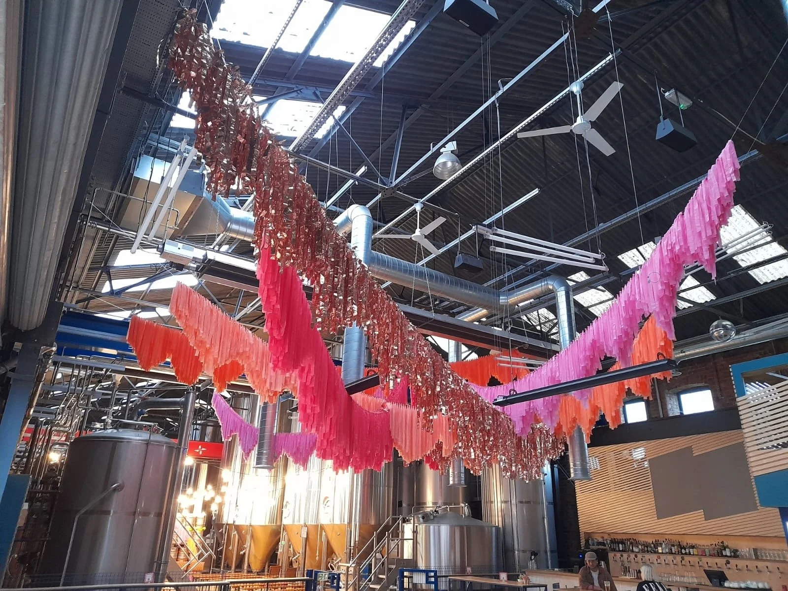 Streamadelica wedding décor inside an industrial brewery venue, showcasing bold pink, orange and metallic hanging installations above stainless steel tanks for a vibrant, creative wedding celebration.