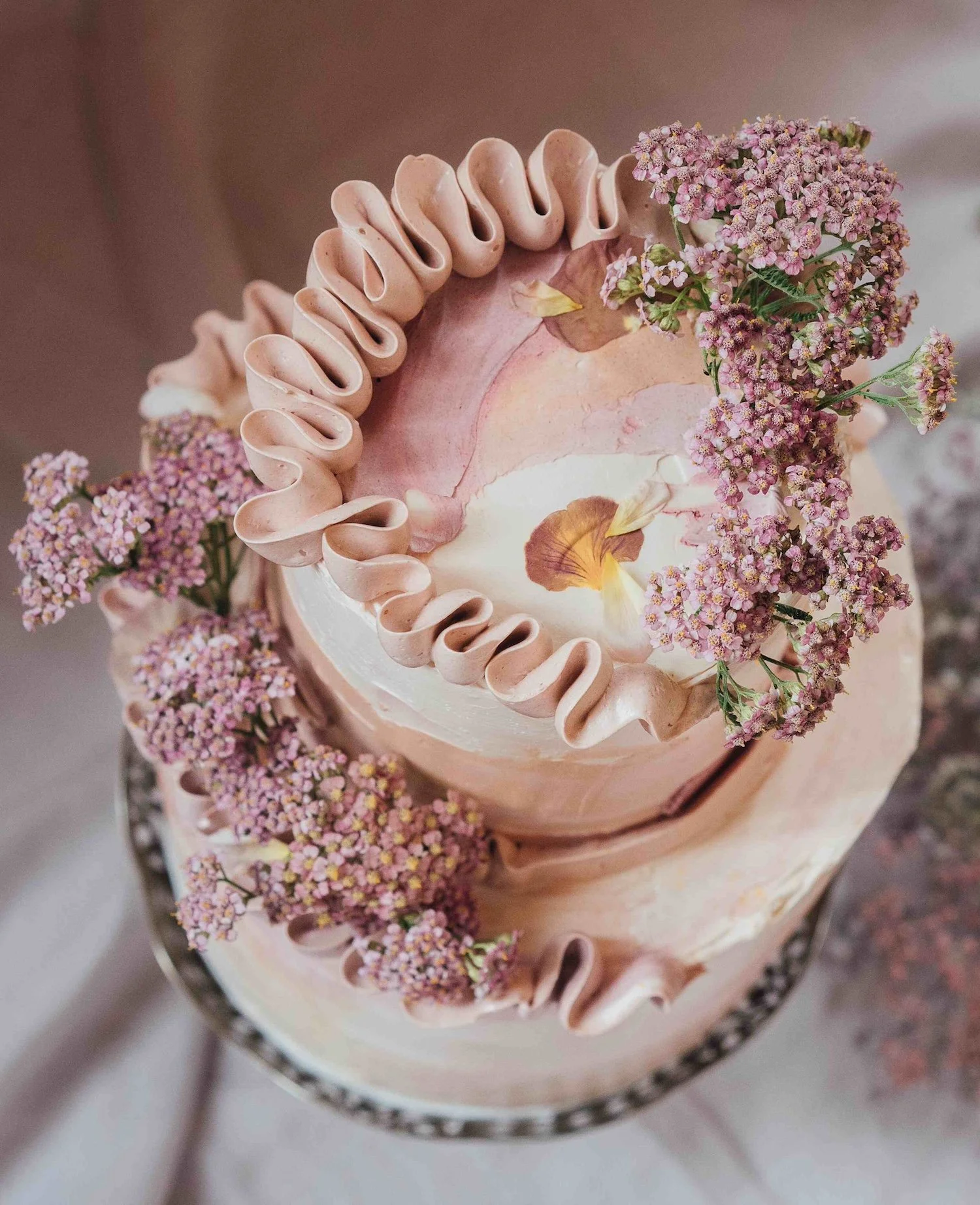 An artistic wedding cake with swirly icing and fresh flowers. The cake has been designed by Sarah and Cake.