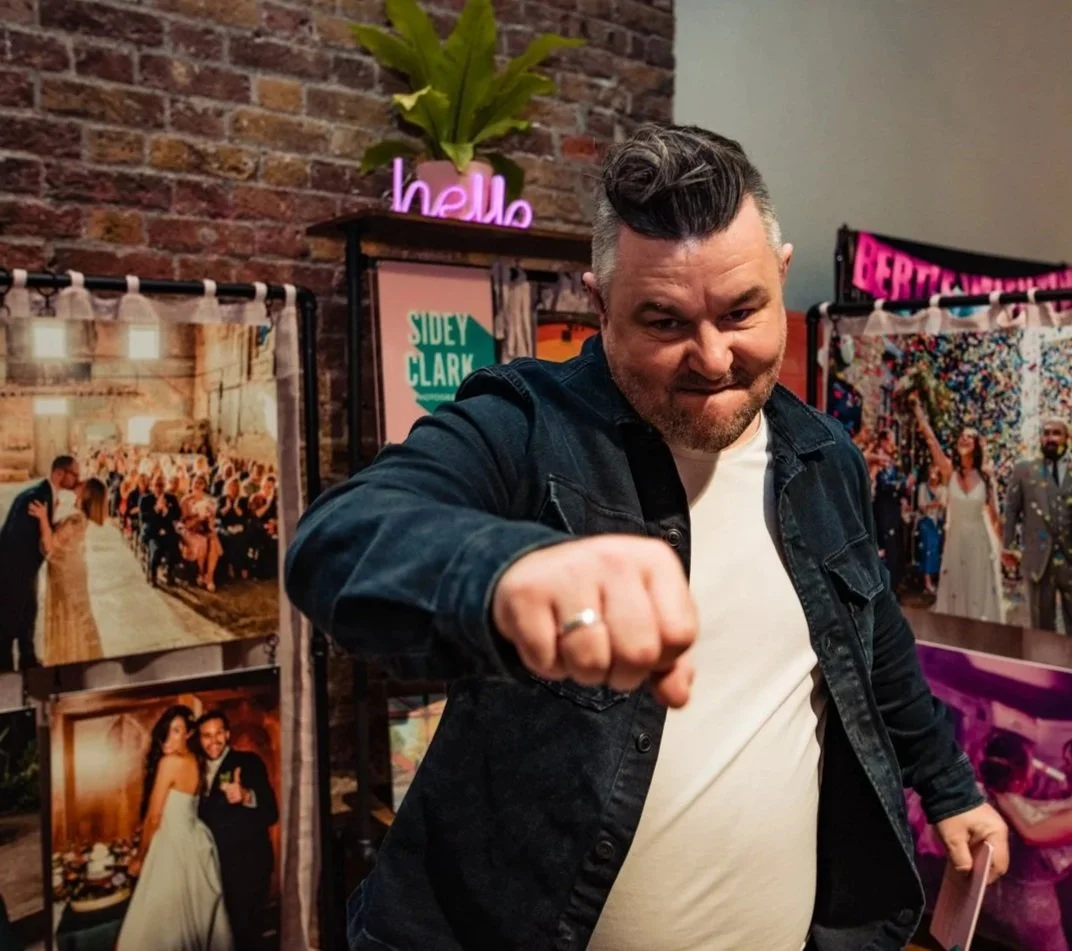 A photographer at a wedding fair is pretending to punch the camera.