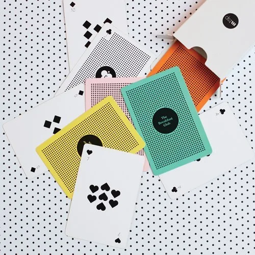 Set of colourful playing cards with bold geometric backs in yellow, turquoise, pink, and orange, designed by Melon Teaspoon as unique party game accessories.