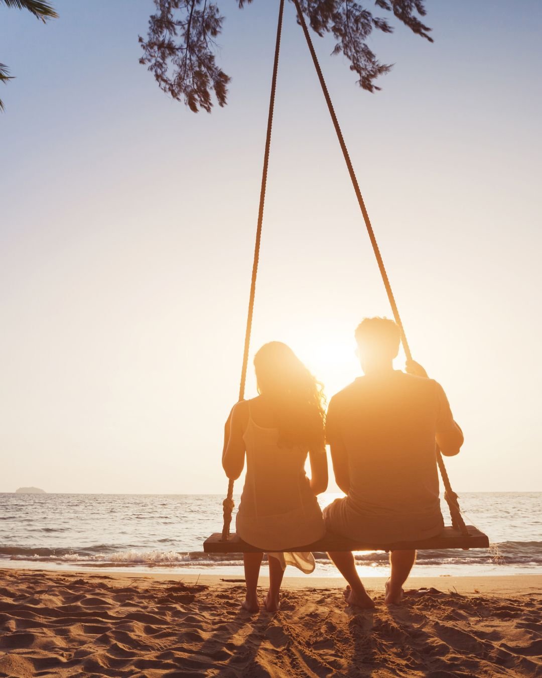 A couple on a swing in the sunset on their honeymoon.