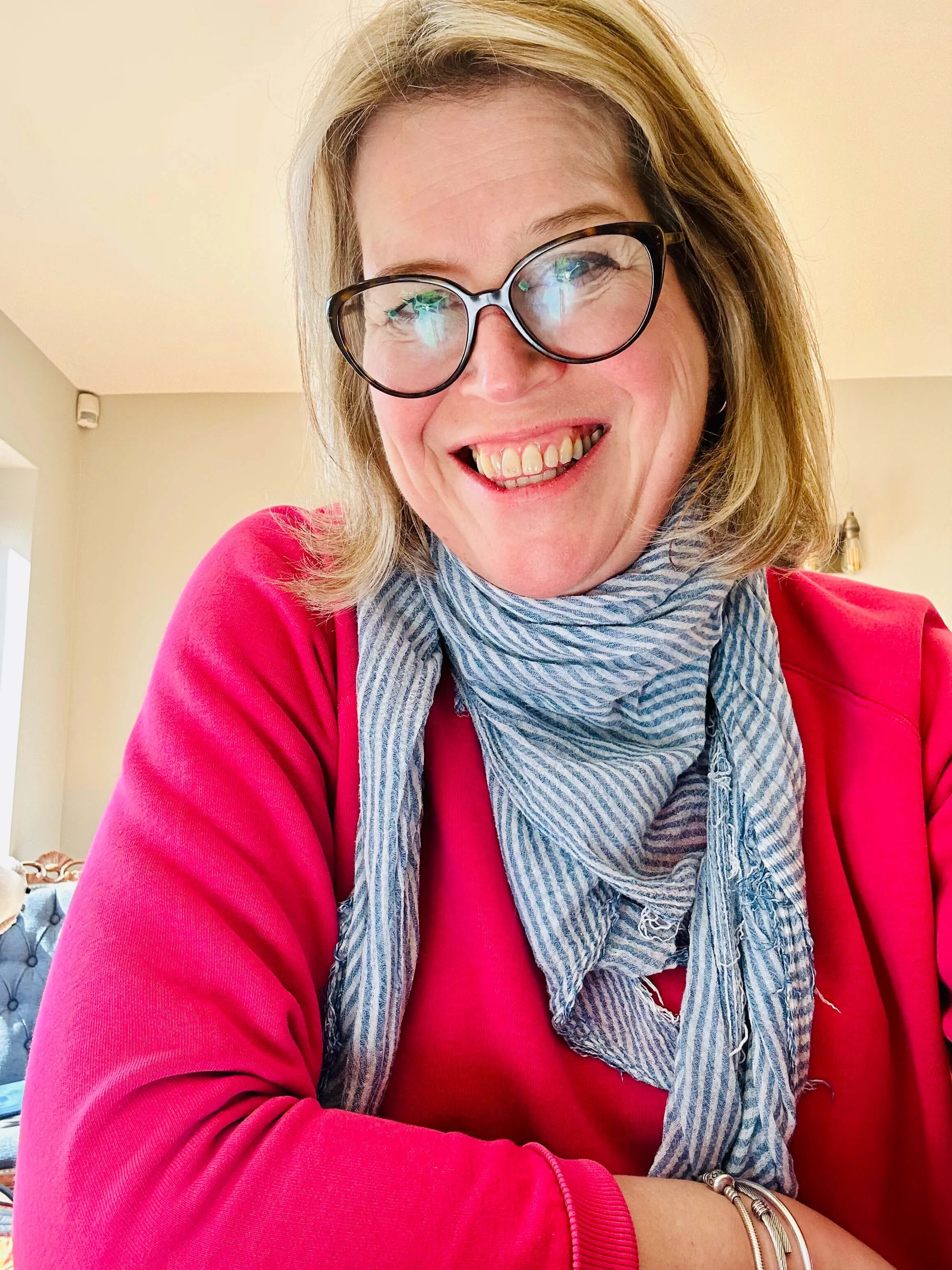 Becky M Celebrant wearing glasses, smiling at the camera, in a pink jumper and stripey neck scarf. 