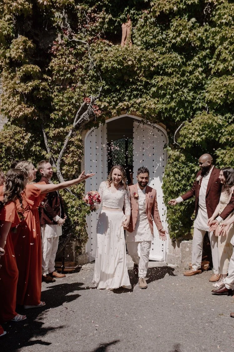 A smiling couple outside their venue, the doorway surrounded by greenery, at their wedding styled by Wild Soul Weddings, eco wedding planners in the UK. 