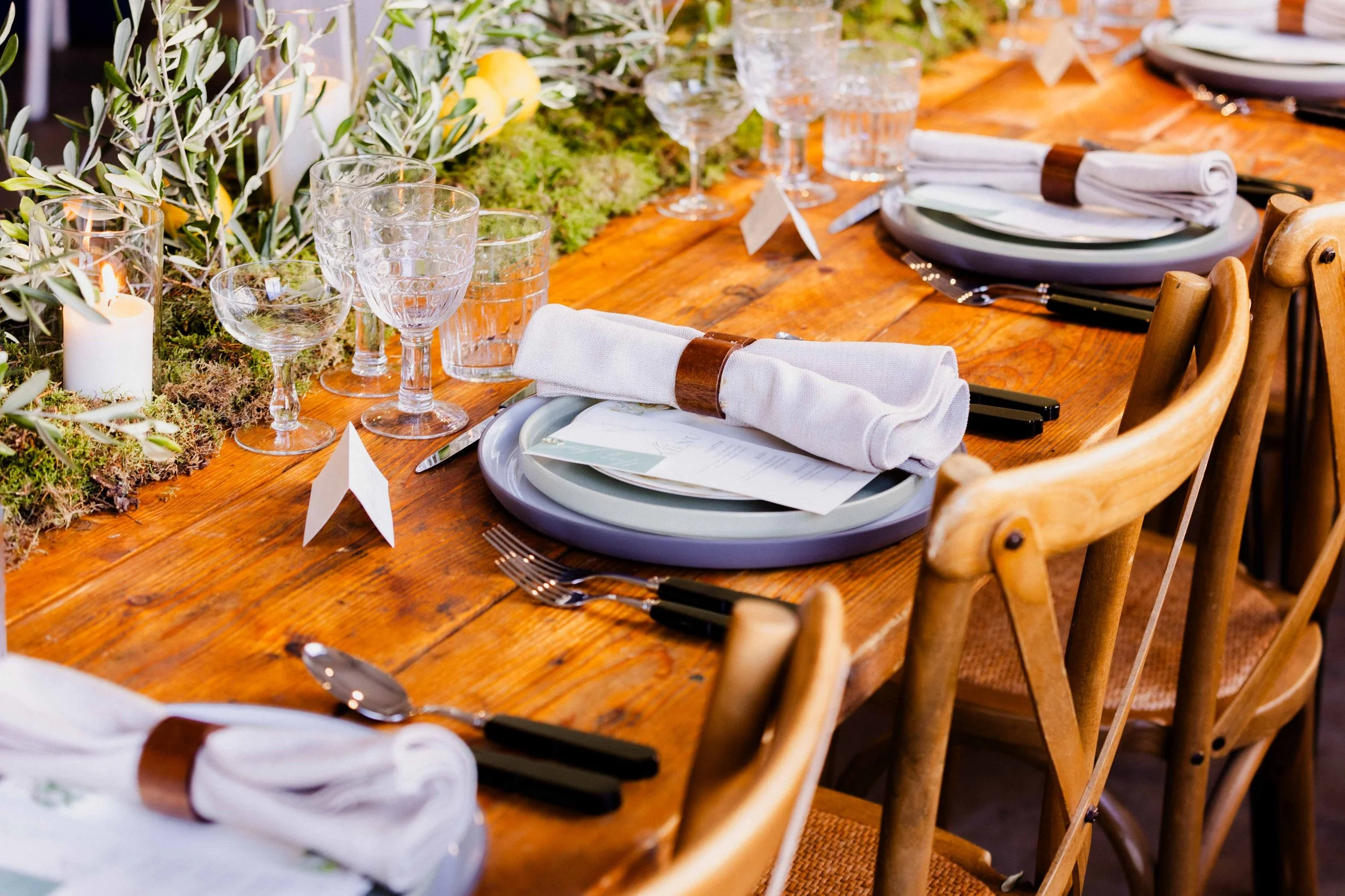 A beautifully styled wedding reception table at Ministry Venues, featuring rustic wooden tables, layered ceramic plates, rolled linen napkins, cut-crystal glassware and natural greenery, creating an elegant yet relaxed tablescape ideal for modern, de