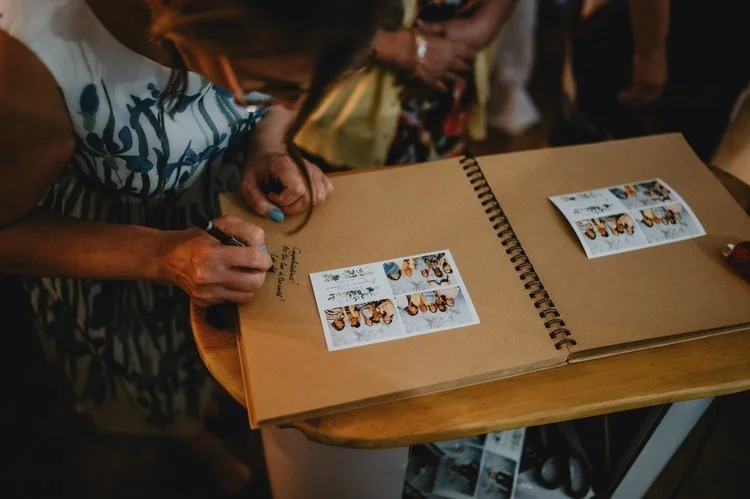 A guest adds photo strips and a handwritten message to a wedding guestbook created with the Flash Fox Photo Booth. This personalised touch lets friends and family share heartfelt notes alongside candid snapshots, creating a keepsake full of fun and m