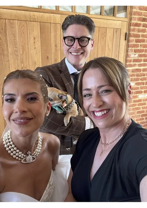 Wedding celebrant Vicky smiling with a newlywed couple and their dog, highlighting her warm and inclusive ceremonies.