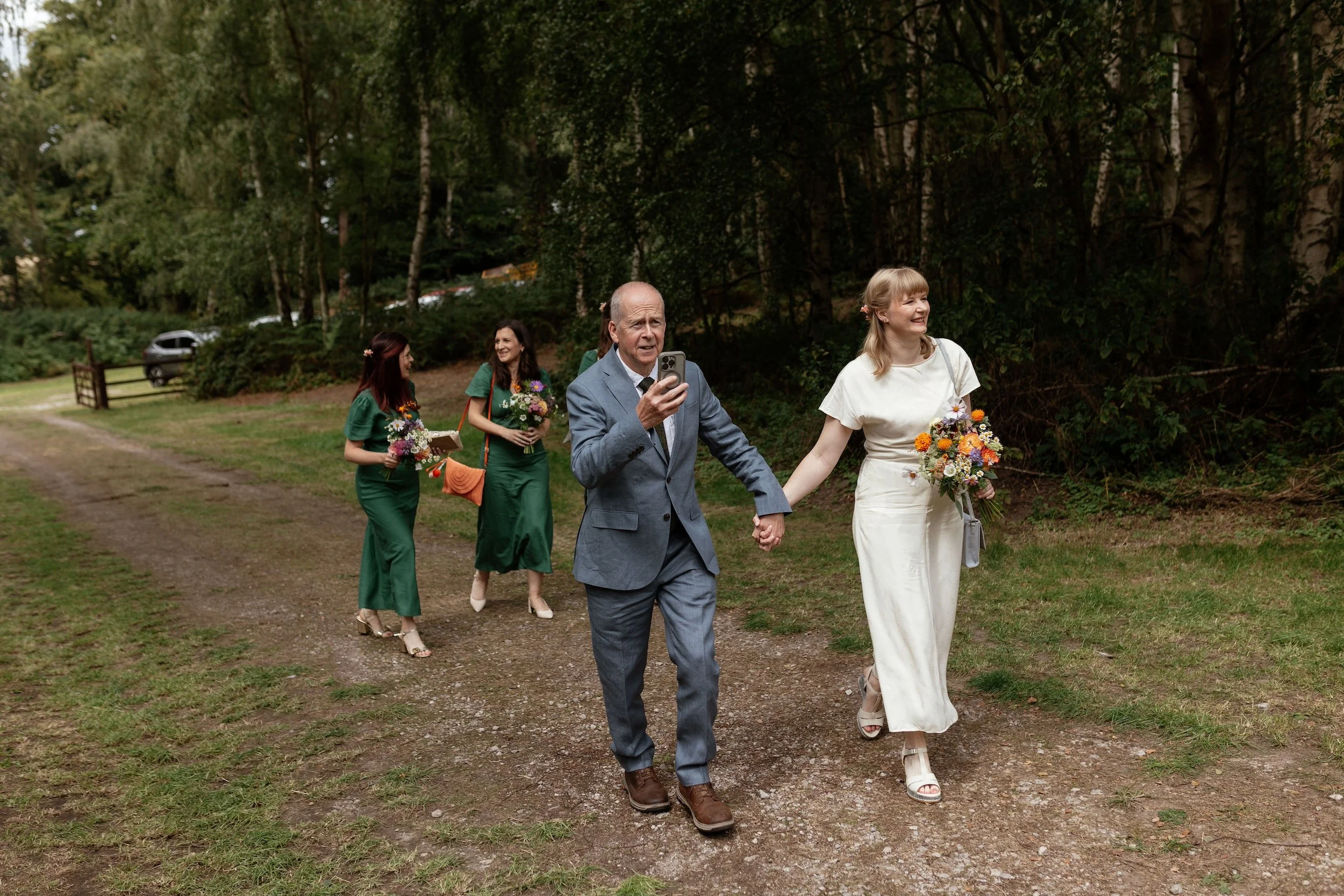 A bride walking through a forest with her dad and bridesmaids.