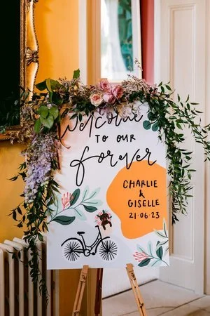 Colourful hand-painted wedding welcome sign by Bee Davies Illustration. Featuring modern calligraphy, floral artwork, and a playful bicycle motif, this bespoke design adds a personal, artistic touch - perfect for creative couples seeking custom weddi