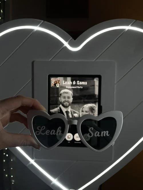 A beautifully lit heart-shaped photo booth creates a romantic setting for Leah and Sam’s engagement celebration. Personalized heart-shaped sunglasses add a sweet touch, reflecting the couple’s names and making a perfect keepsake. The warm glow and mo