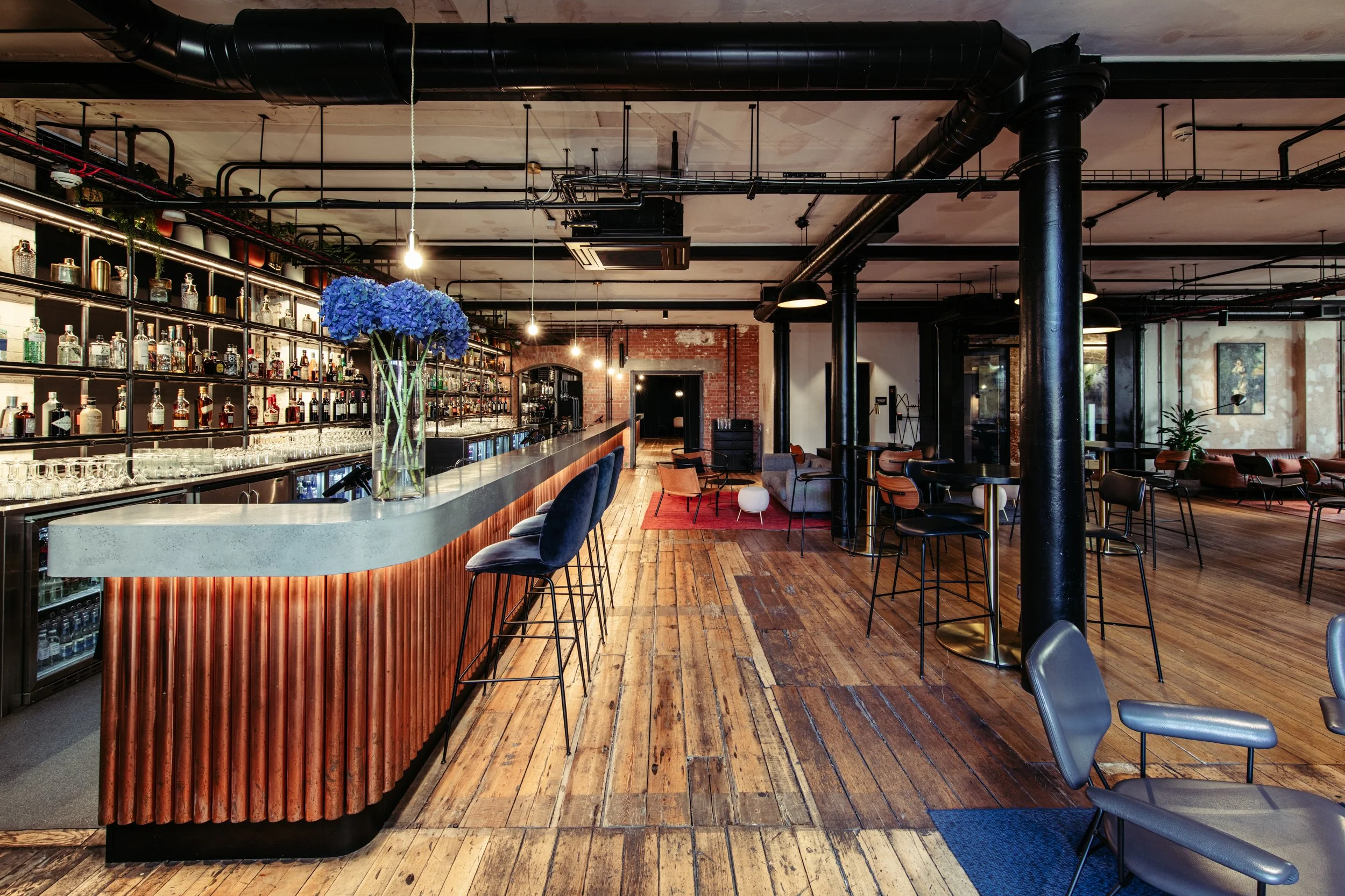 A sophisticated industrial-style bar inside Ministry Venues, featuring exposed brickwork, polished wooden floors, black steel columns and a statement marble-topped bar, creating a stylish and atmospheric setting ideal for modern London weddings, cock