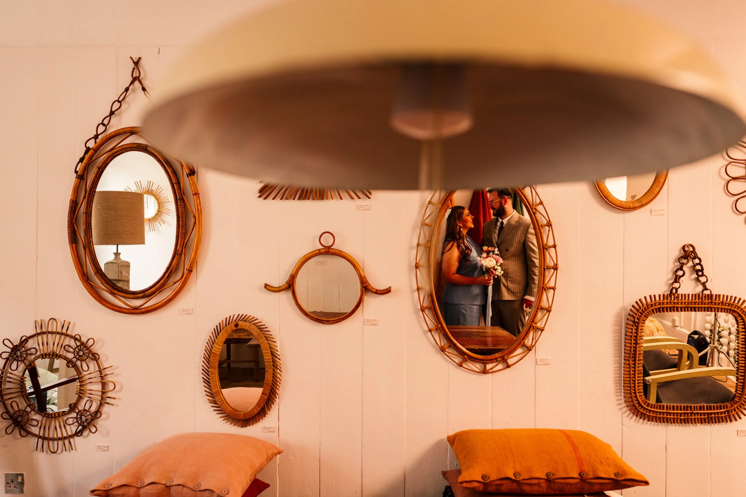 A creative wedding portrait captured in a vintage interior at Townhouse Winchester, where the couple’s reflection appears framed inside a retro rattan mirror. Styled cushions, wicker mirrors, and warm ambient lighting create a cosy, design-led backdr