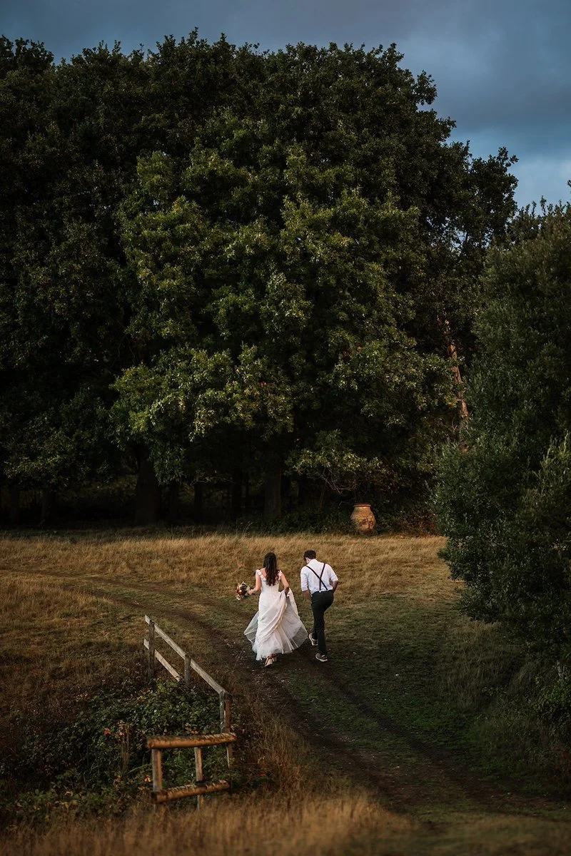 A newlywed couple walk along a woodland path, capturing a free-spirited, nature-led wedding experience planned by Wild Soul Weddings, eco wedding planners in the UK. Rach Elizabeth Photography.