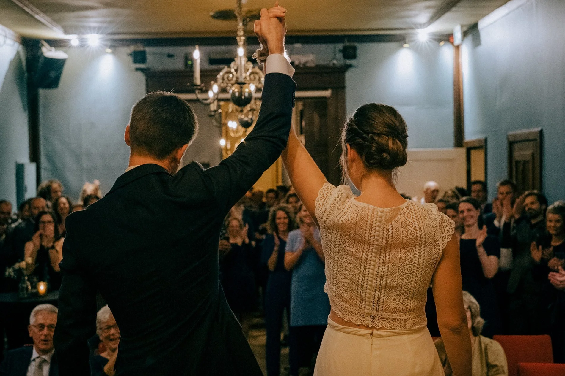 A newly married couple raise their hands in celebration as guests applaud, capturing a joyful, emotional ceremony moment by Quiet Mornings Wedding Photography in Scotland.