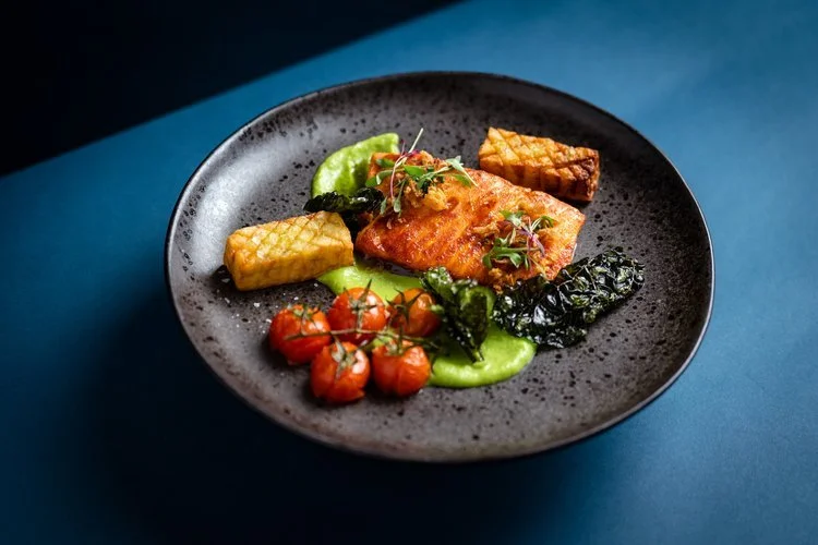 A beautifully plated salmon dish by Hardy’s Catering, featuring crispy-skinned salmon served with roasted cherry tomatoes, golden potato cubes, green pea purée, and sautéed greens. This elegant presentation showcases Hardy’s creative flair and fine d