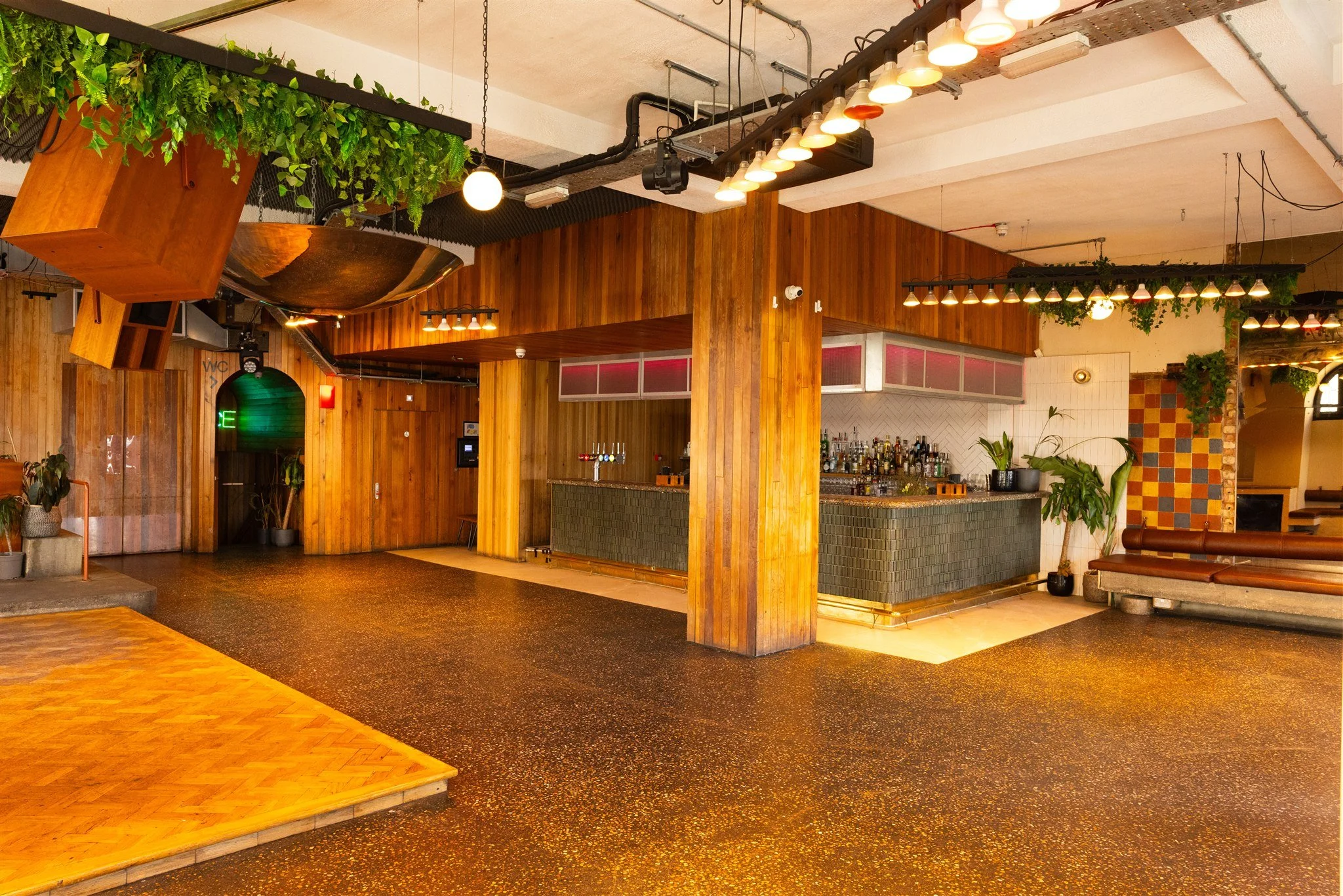 Bright modern interior of Pier Court, a Brighton wedding venue featuring warm wooden paneling, contemporary lighting, statement hanging greenery and a stylish tiled bar area. The spacious open-plan layout is ideal for wedding receptions, parties and 