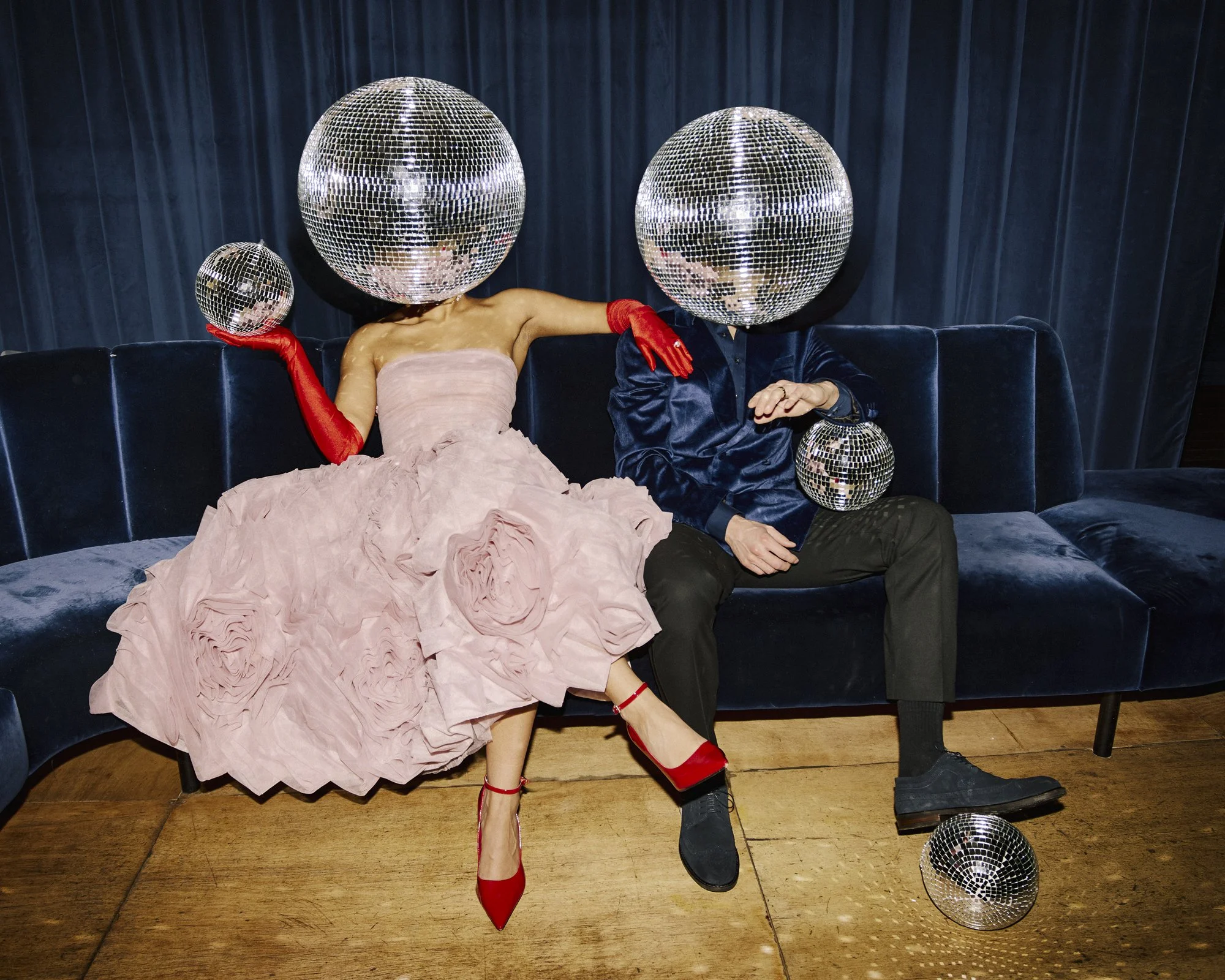 A stylish couple relax on a velvet sofa at Ministry ‘I Do’, a modern London wedding venue, wearing formal attire with mirrored disco balls for a playful, nightlife-inspired wedding photo that reflects the venue’s bold, contemporary atmosphere.