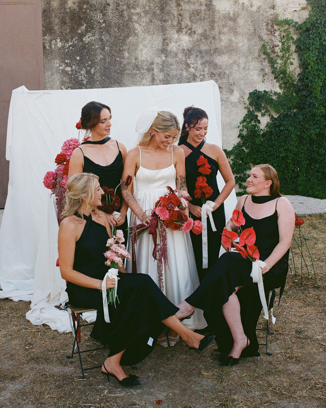 A modern bride is standing with her bridesmaids and they are all wearing black bridesmaid dresses from Rewritten London.
