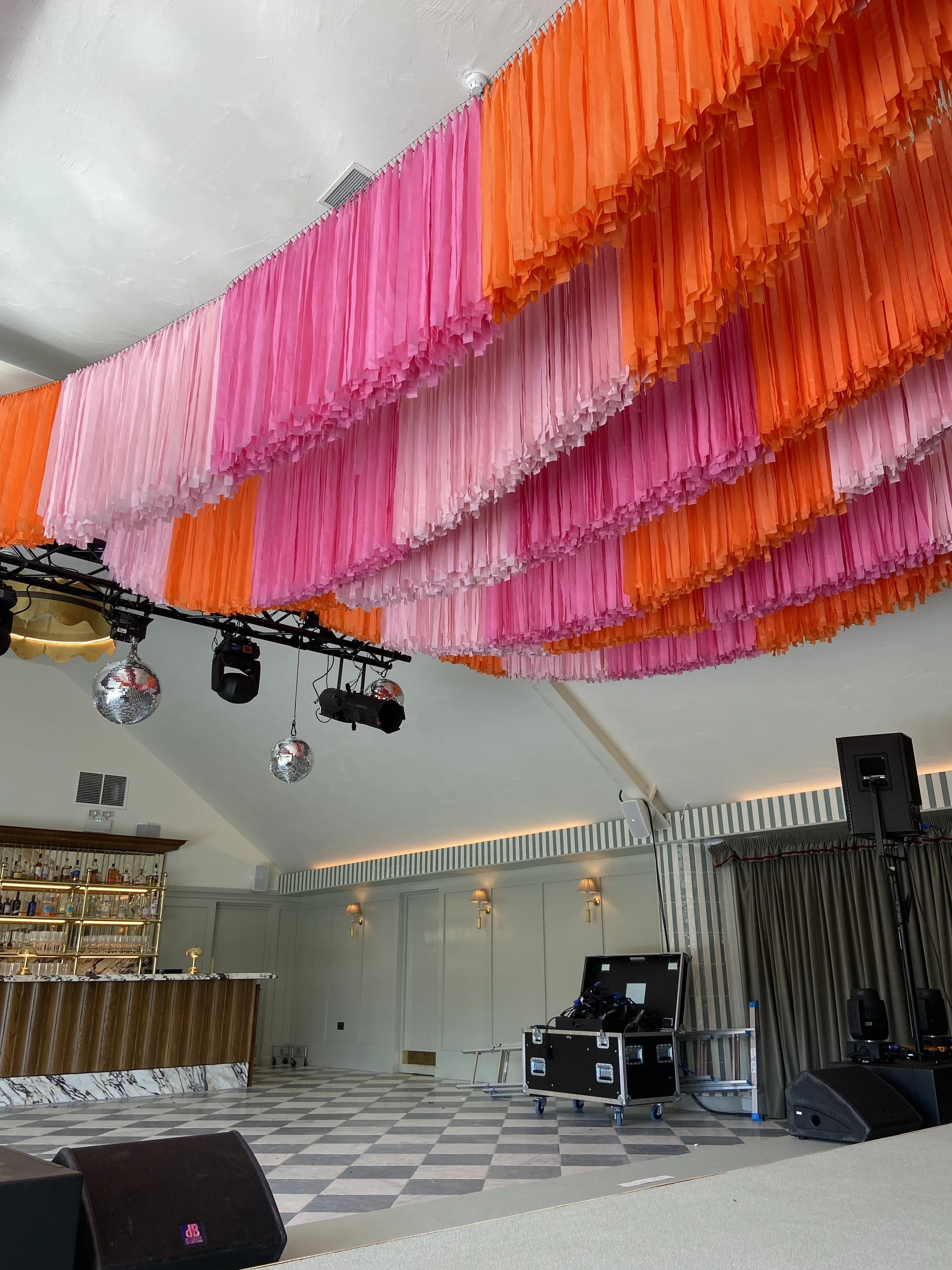 Streamadelica wedding décor installation with flowing pink and orange fringe ceiling, adding bold colour, texture and a modern festival feel to an elegant indoor reception and dancefloor space.