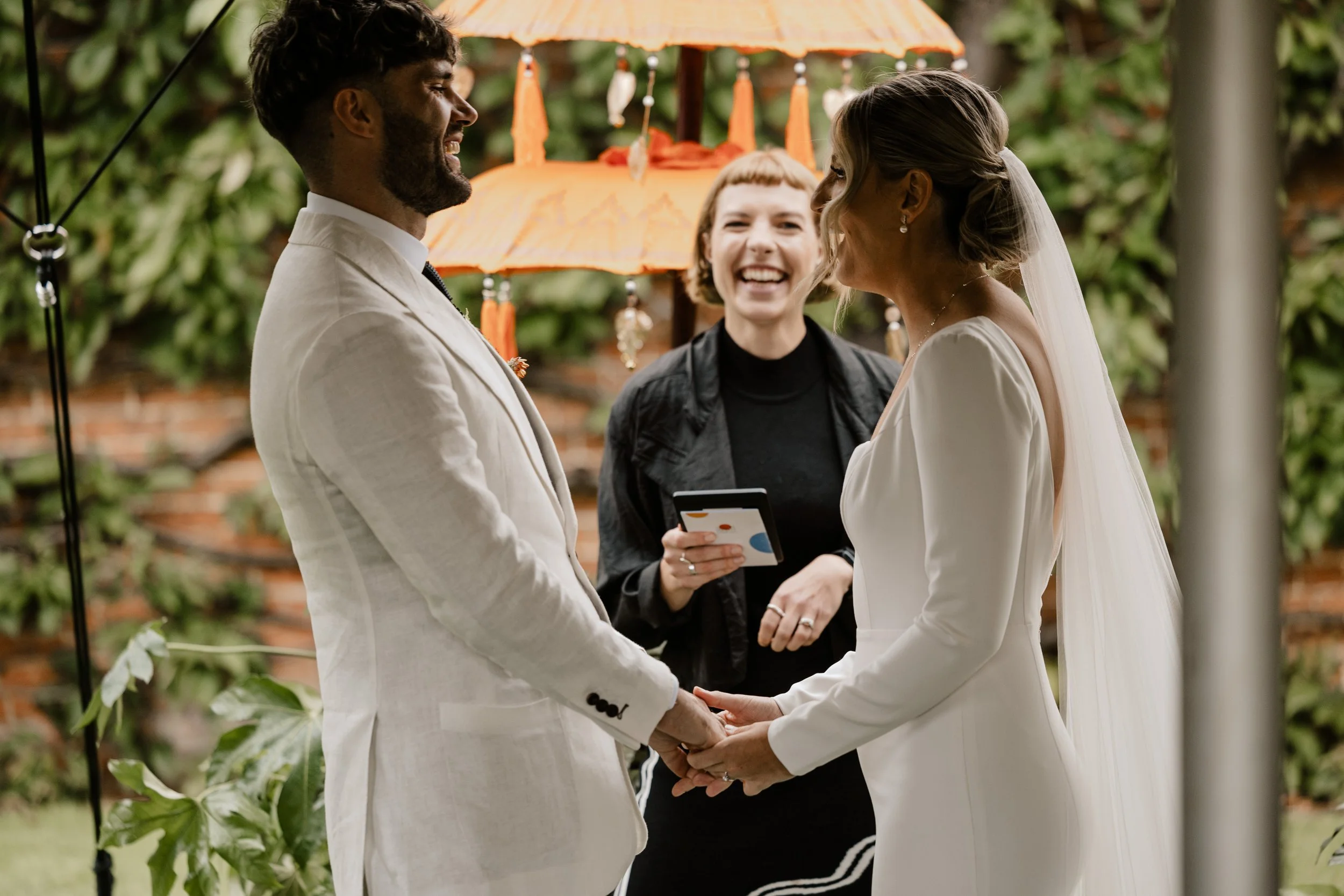 Tab Taylor from Say it Right Ceremonies conducts a wedding. The couple wearing white, share an amusing moment with the celebrant.