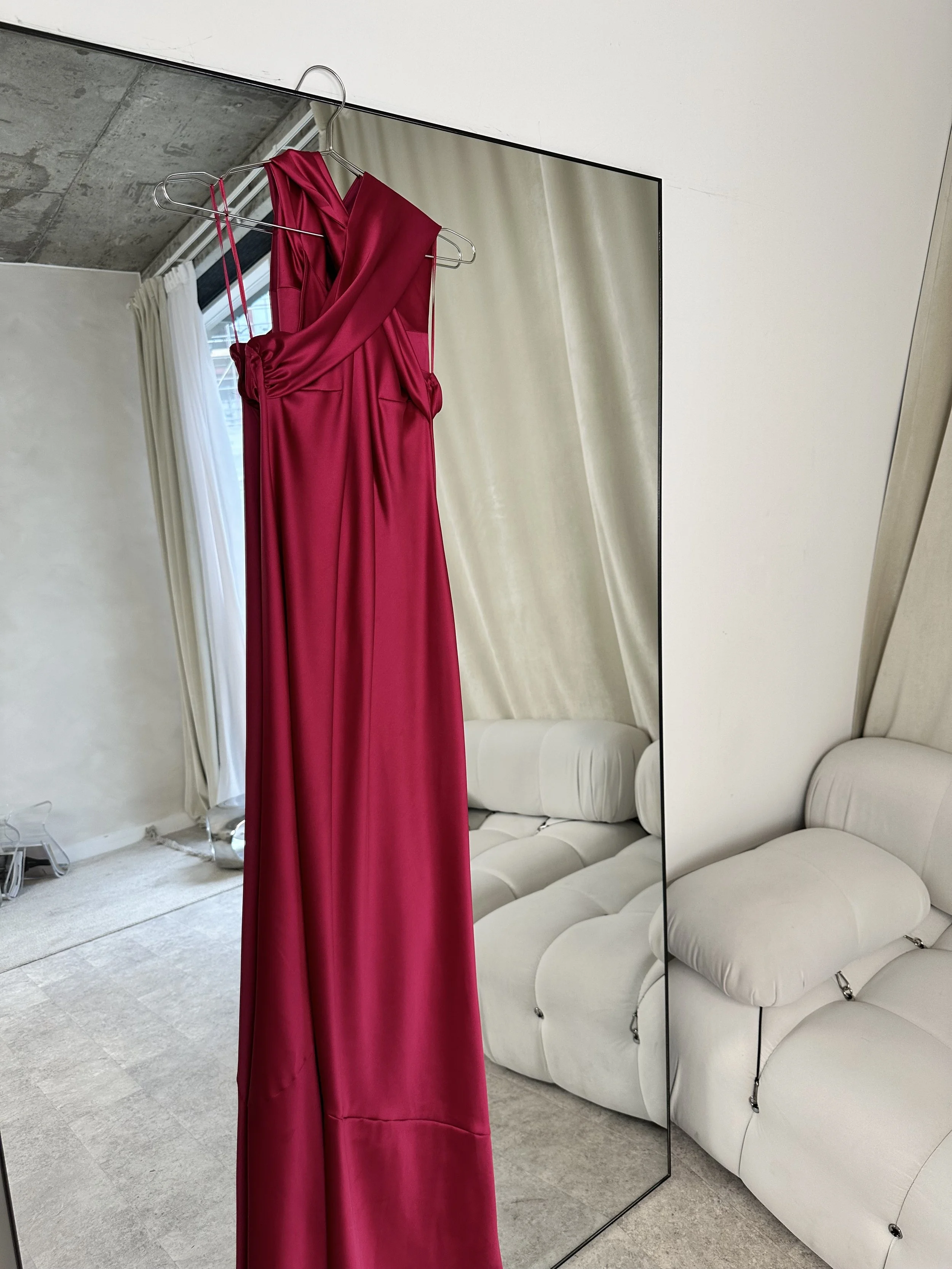 A pink bridesmaid dress hanging up on a mirror.