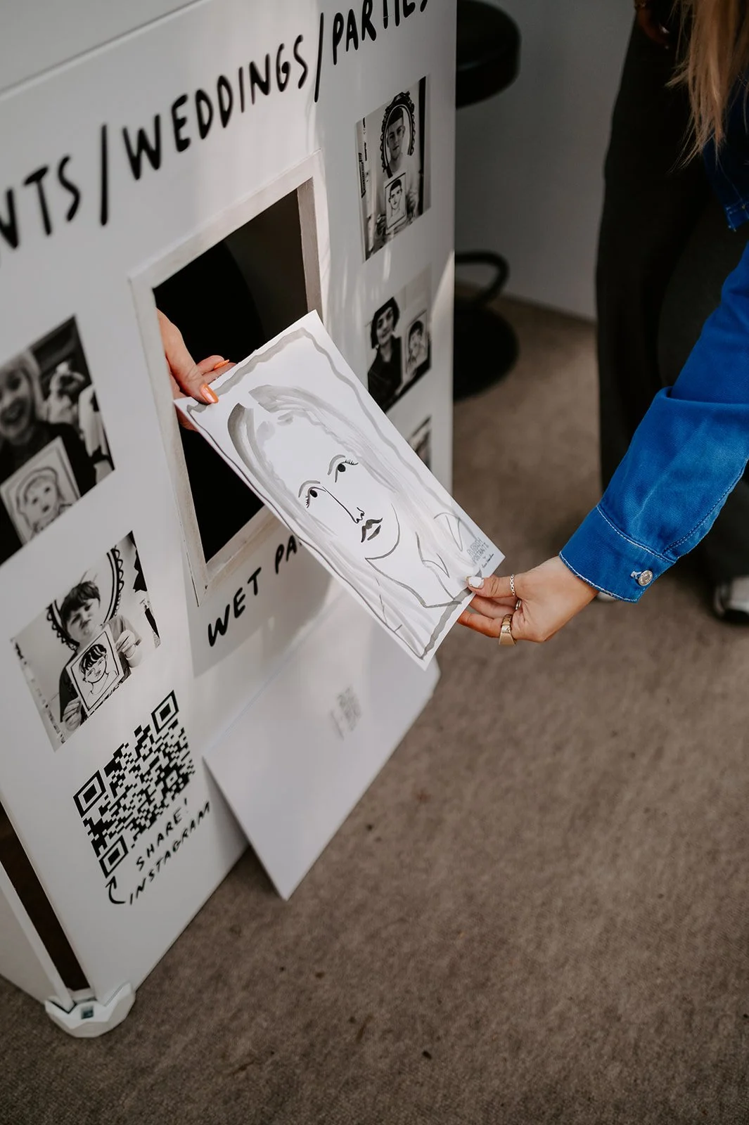 A freshly painted portrait being handed through the small window of the Rubbish Portraits booth captures the magic of Lucie Sheridan’s unique live art experience. Guests receive their one-of-a-kind ink illustration within minutes, making it a charmin