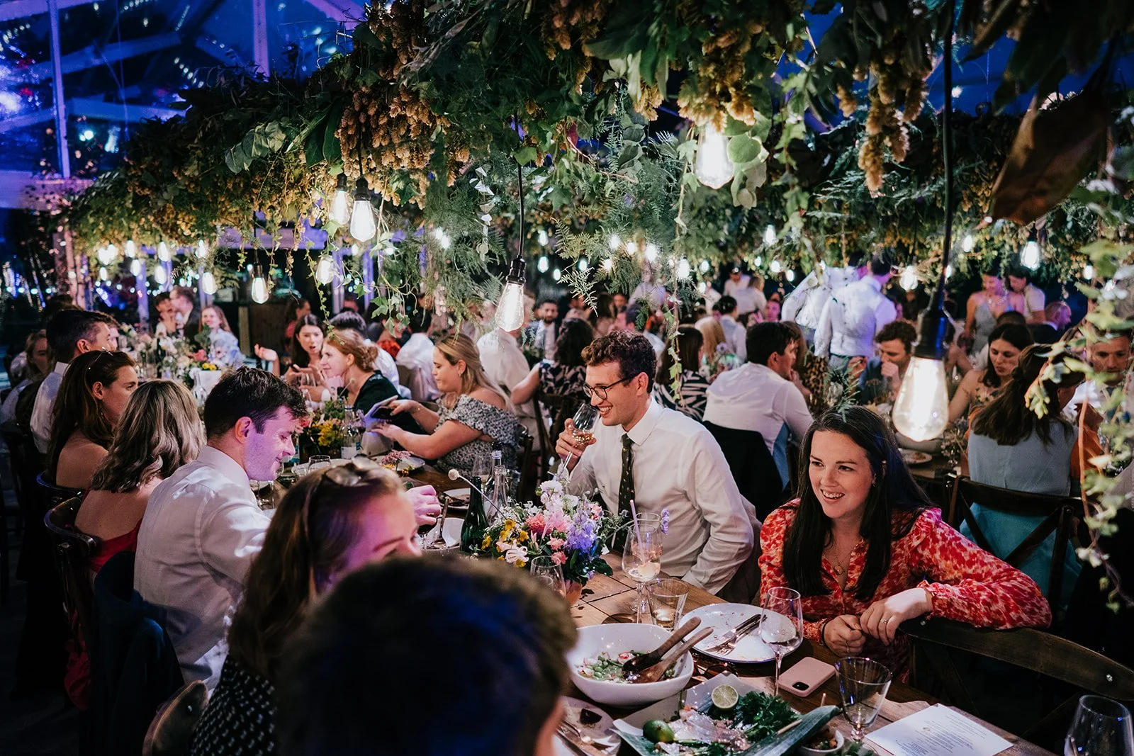 A vibrant outdoor wedding moment featuring colourful ribbon streamers flying above a joyful crowd as two guests laugh and celebrate beneath a blue sky. Shot by Alan Law Photography, this image captures energetic festival-style wedding vibes with bold
